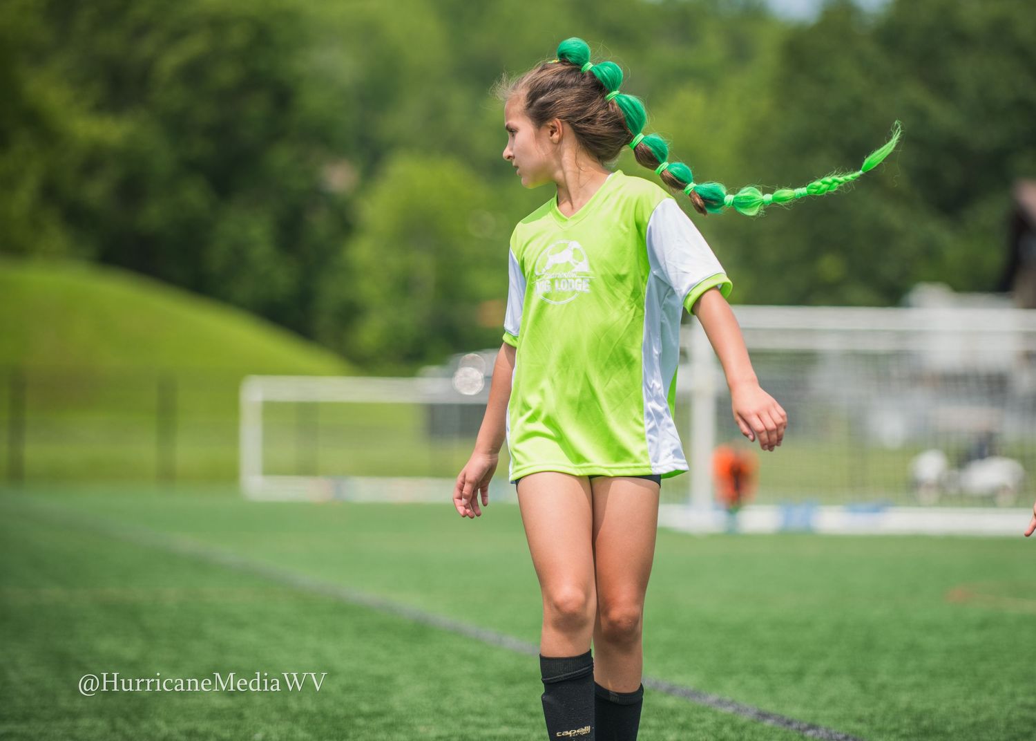 Soccer player in neon green uniform with braided hair runs on grass field.