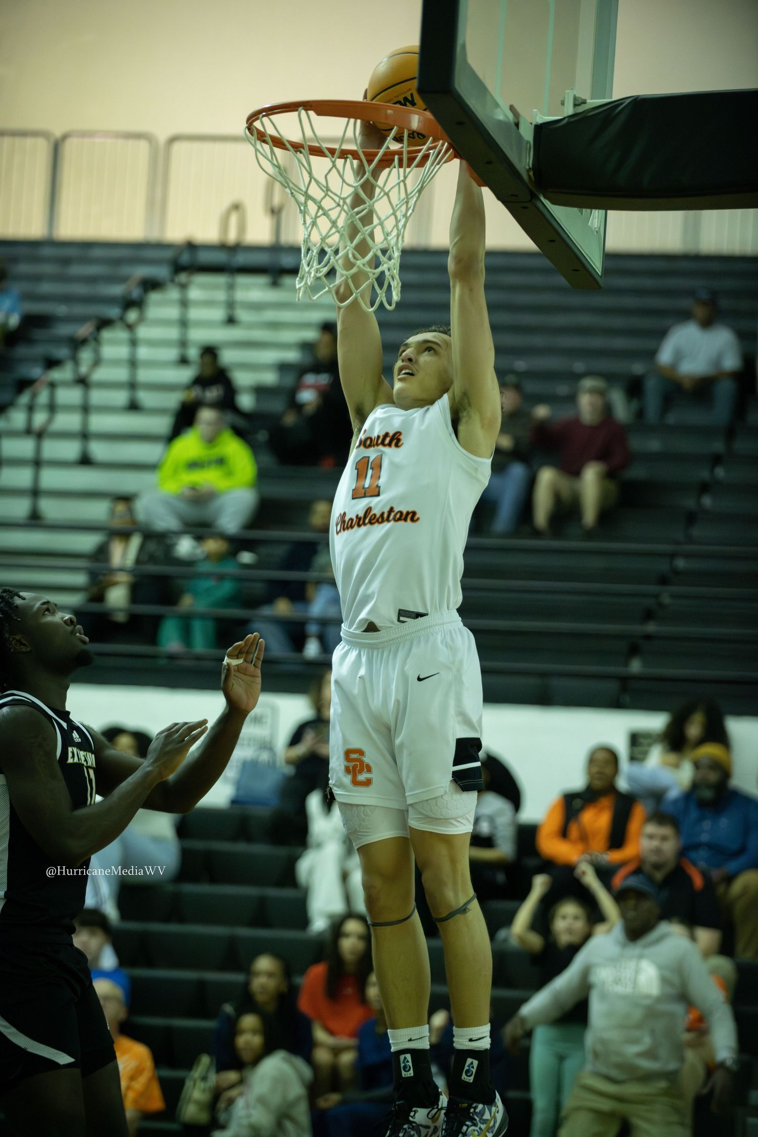 Basketball player in white uniform dunking ball during game with crowd in background.