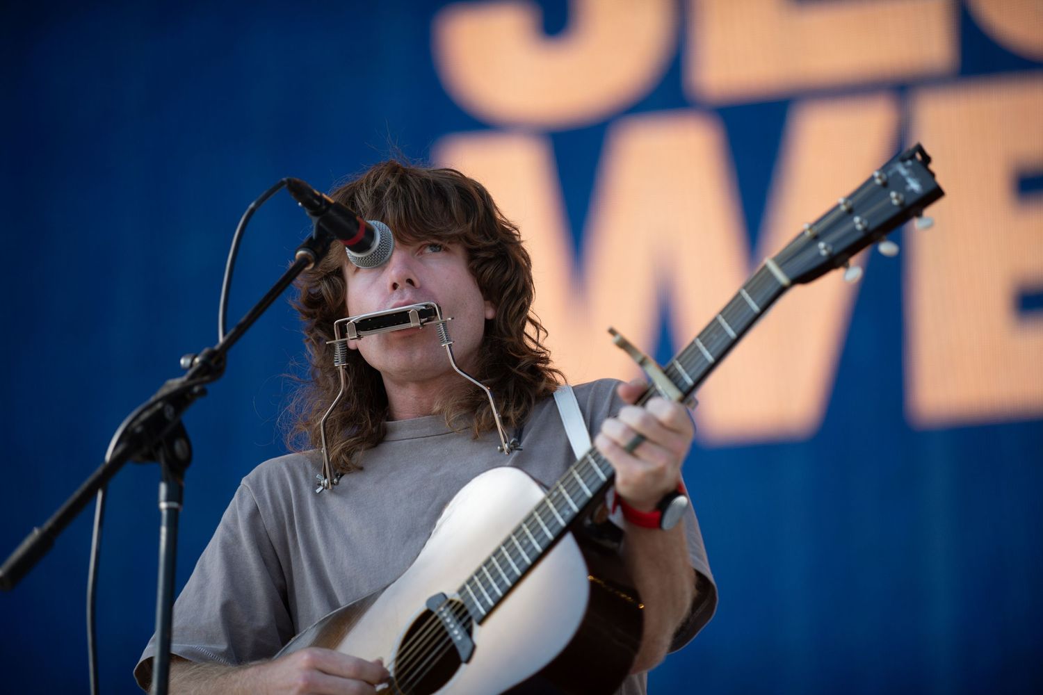 A musician performs on stage with a banjo against a dark blue background during a concert performance.