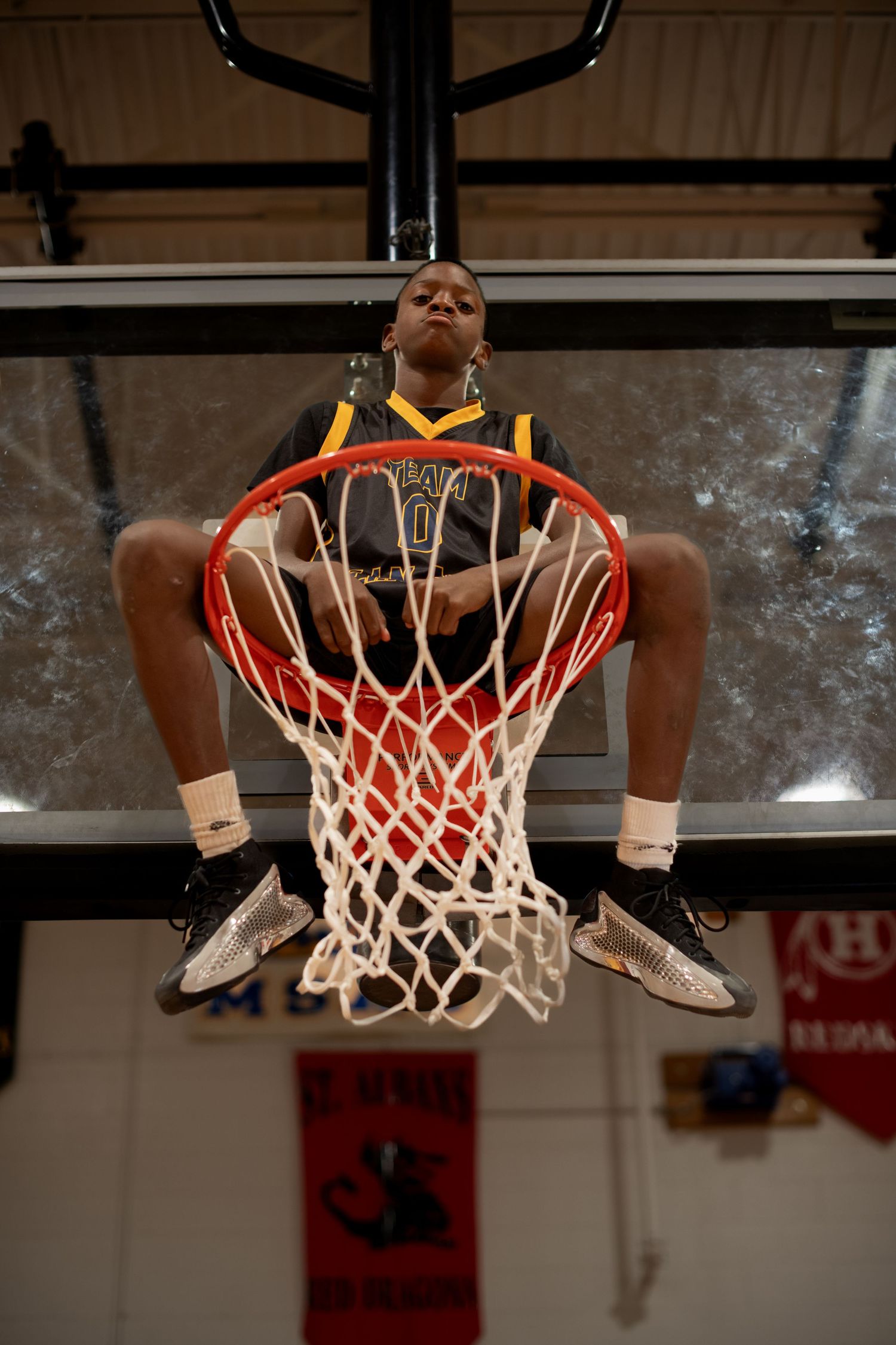 Basketball player sitting on hoop rim in dramatic low-angle shot.