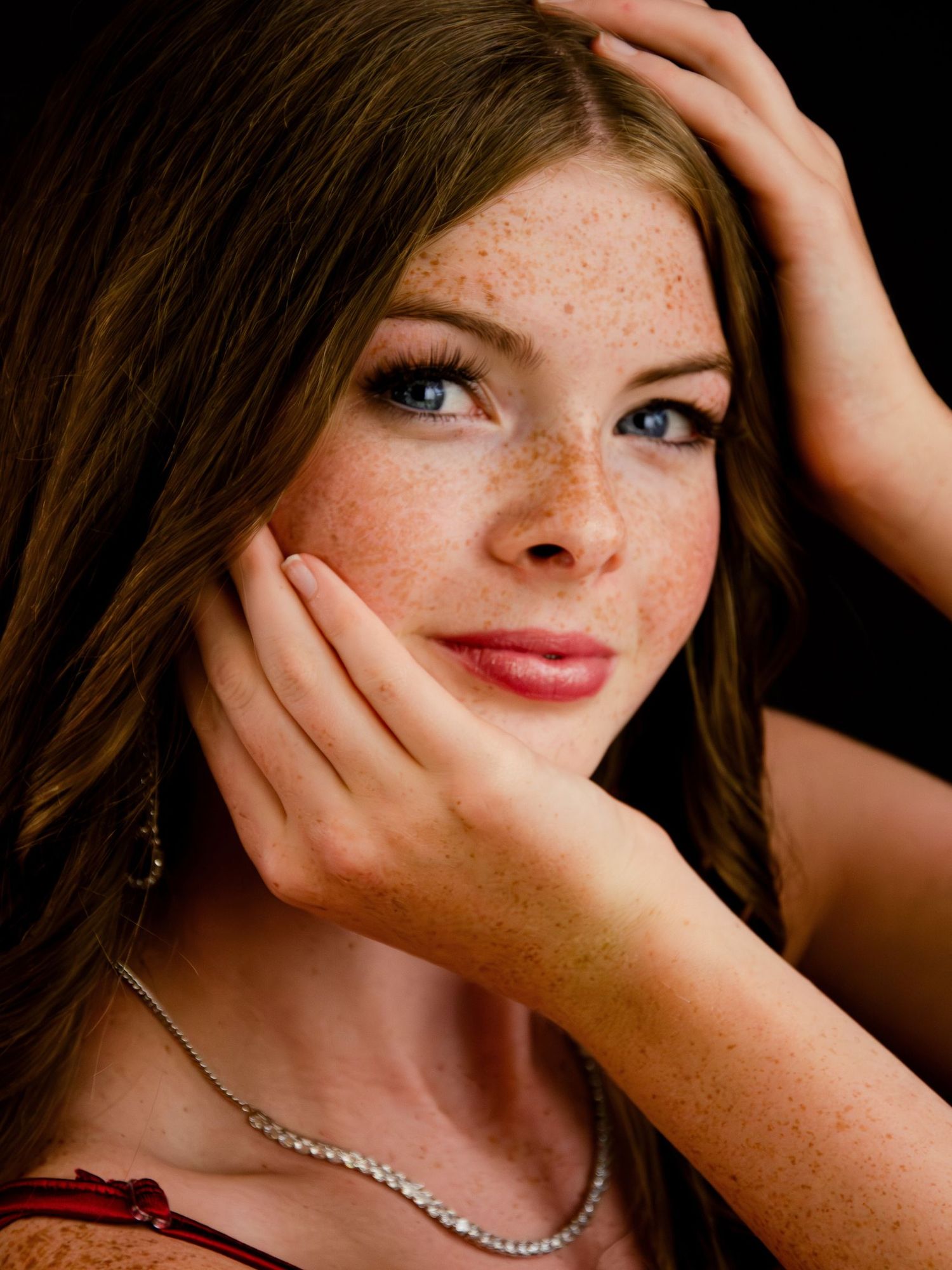 Artistic close-up portrait with hands framing face against dark background with dramatic lighting.