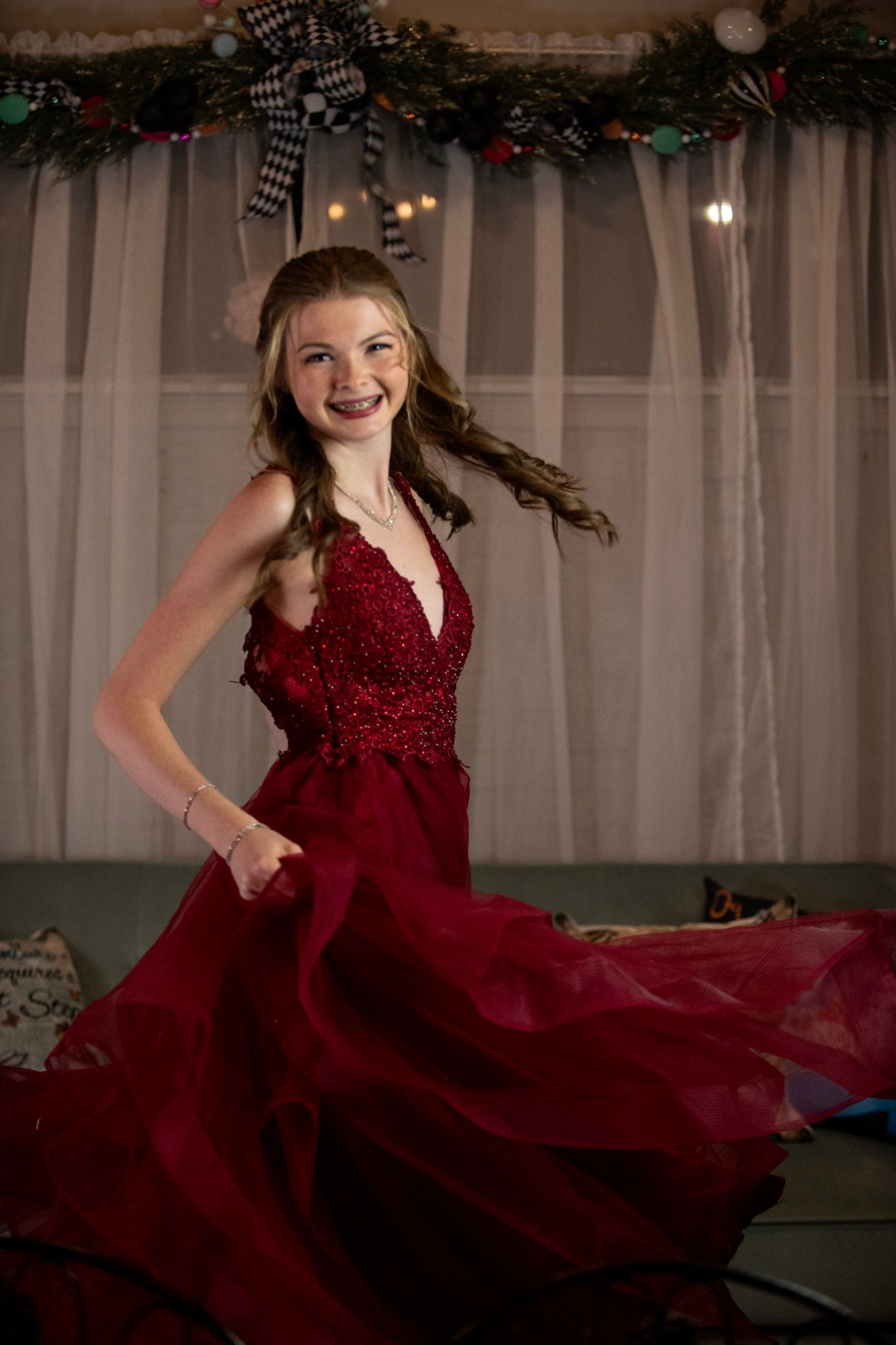 Elegant spin in flowing red formal dress against decorated holiday backdrop.