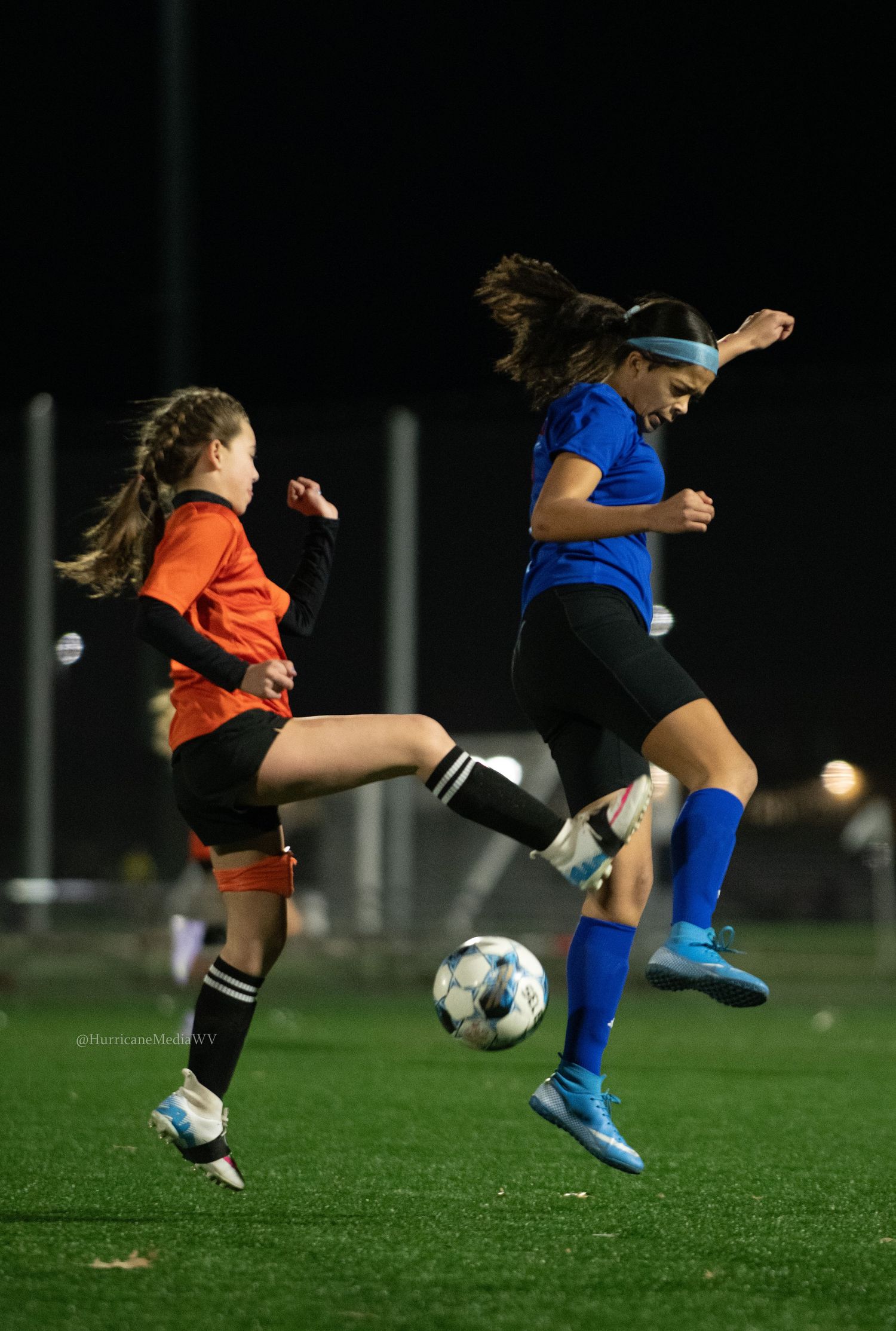 Two soccer players leap for ball during competitive nighttime match action.