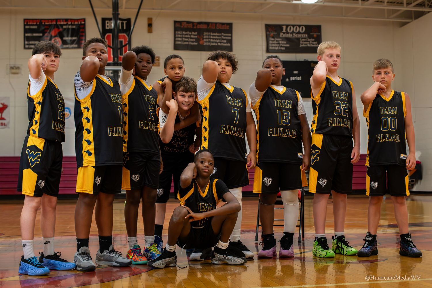 Basketball team in black and yellow uniforms poses for team photo in gymnasium.