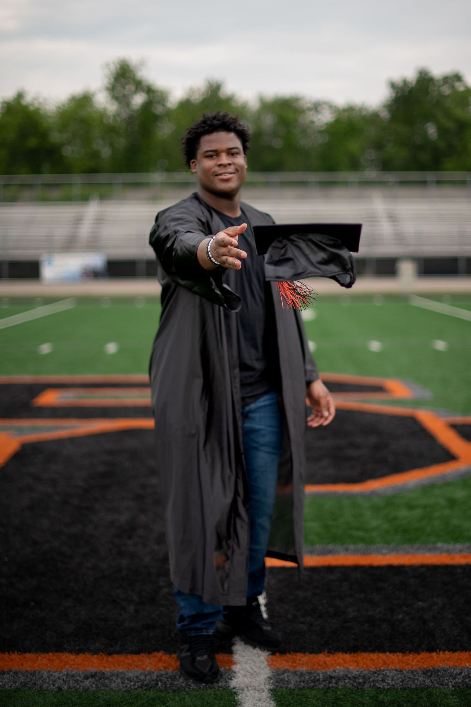 Person wearing a graduation gown poses for photos on a sports field with orange markings.