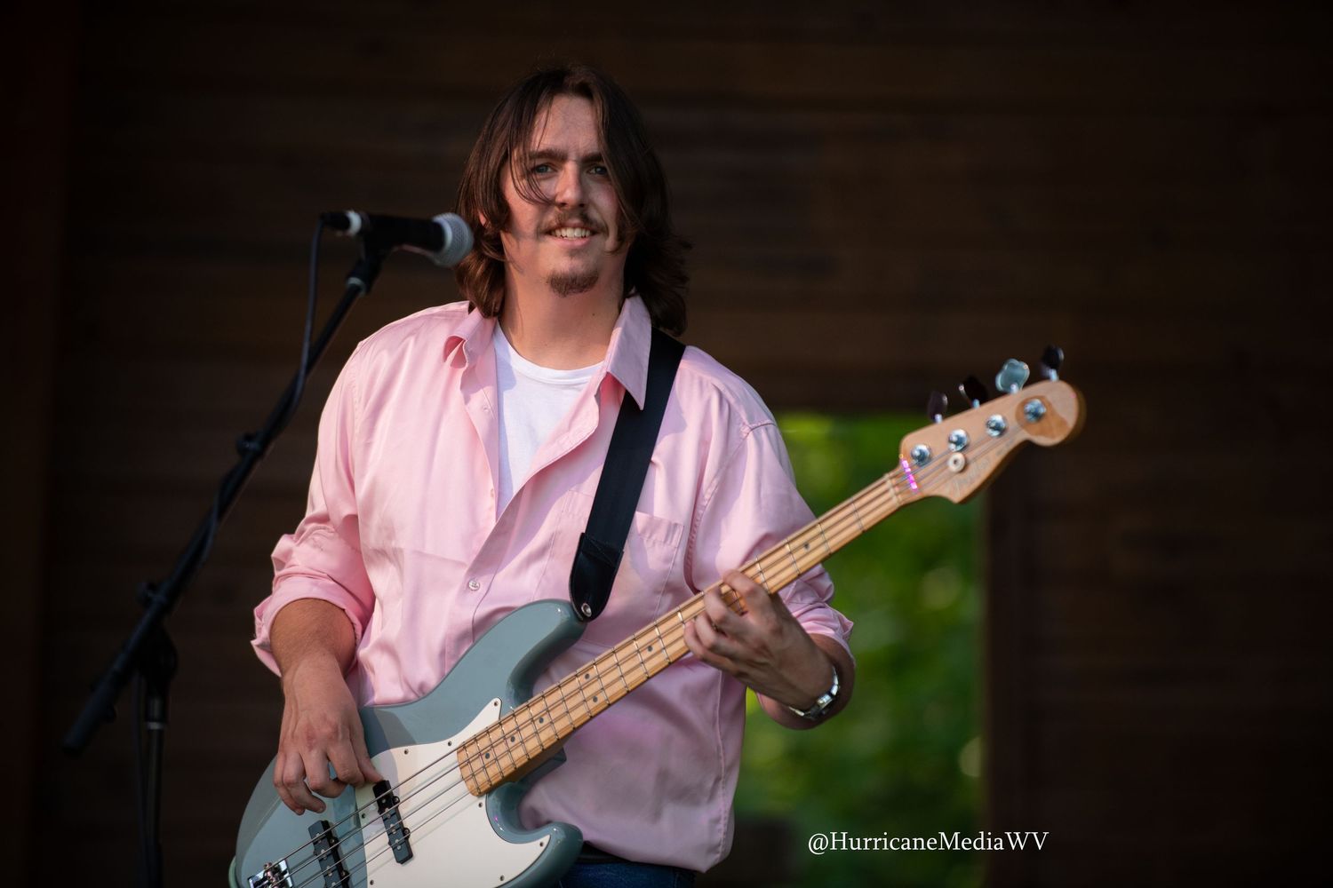 Bassist performs on stage with electric bass guitar in dimly lit concert setting.