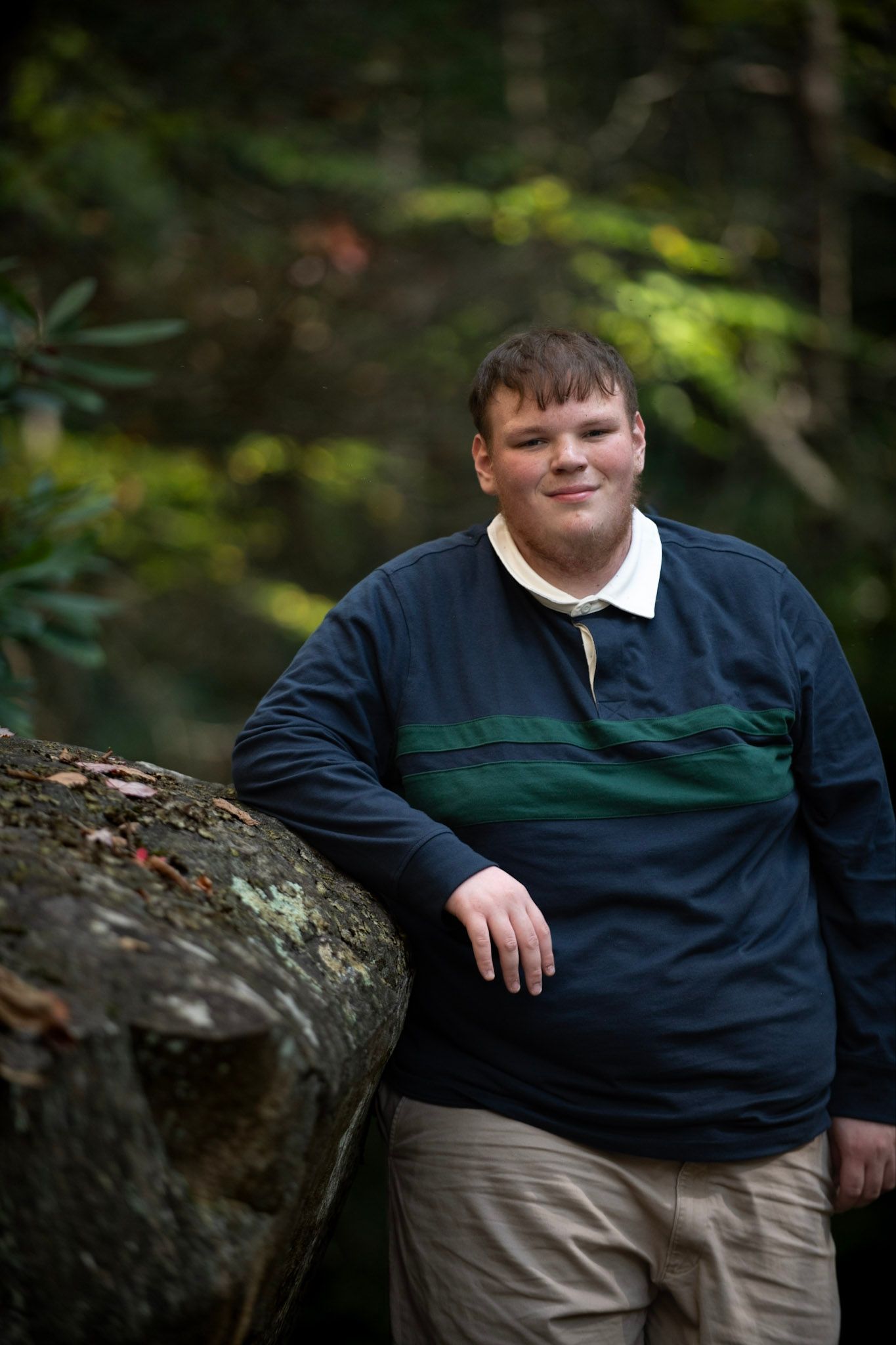 Portrait against natural forest background wearing navy and green striped polo shirt.