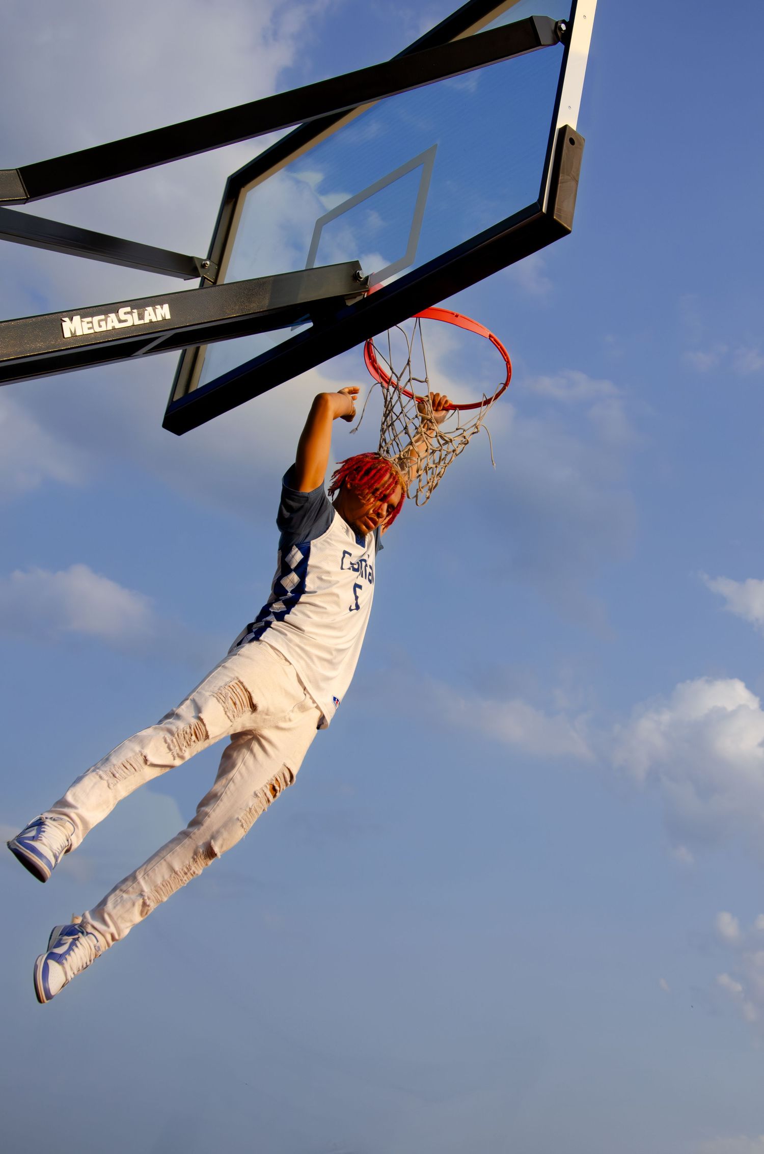 Basketball player dunking on outdoor court against blue sky.