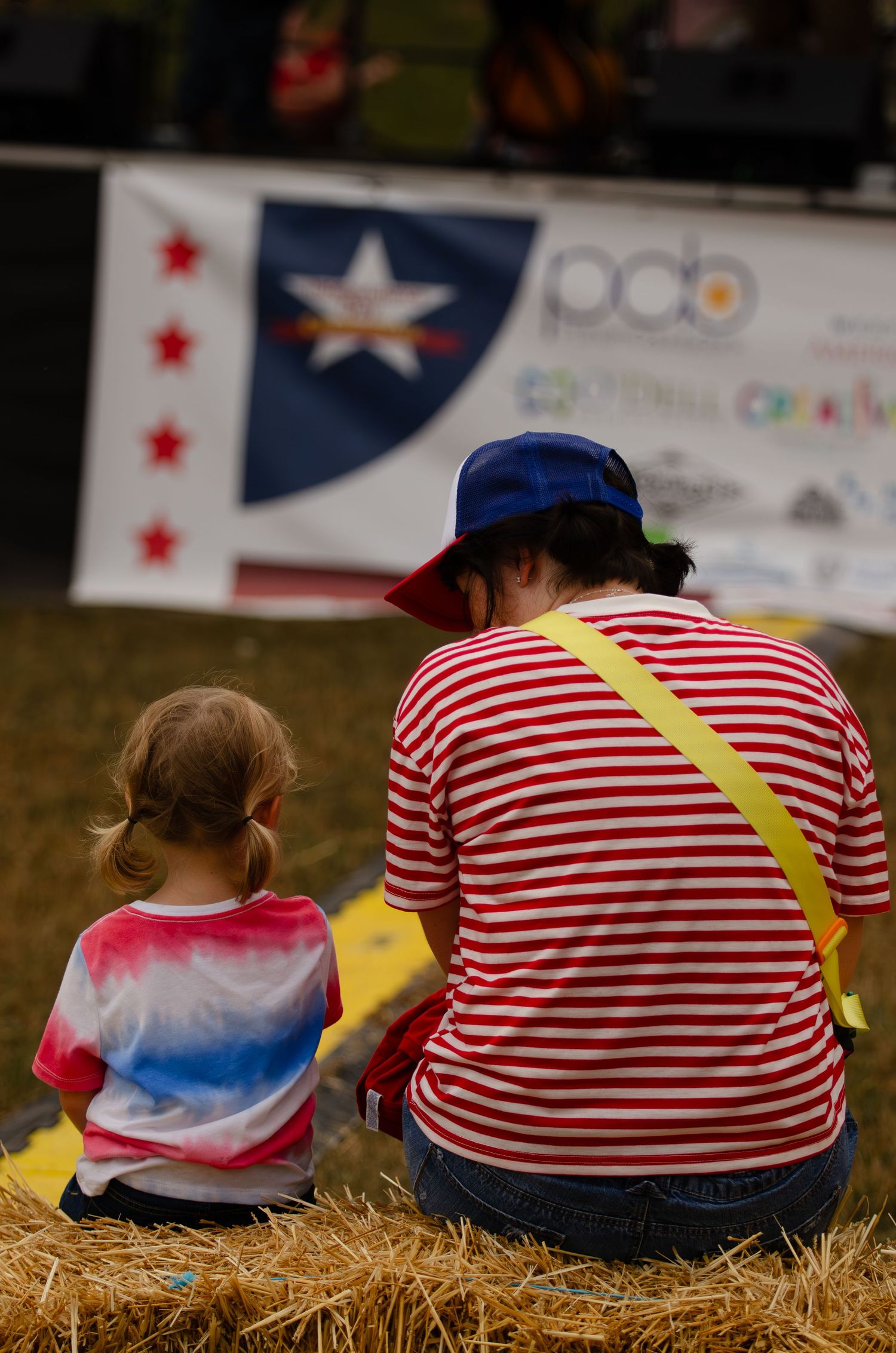 People sitting on hay bales wearing red and white striped shirts at an outdoor event.