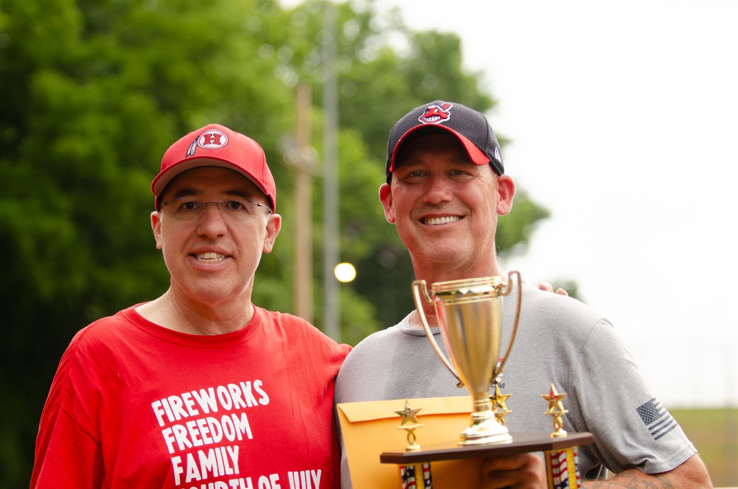 Two participants hold a trophy at an outdoor summer event.