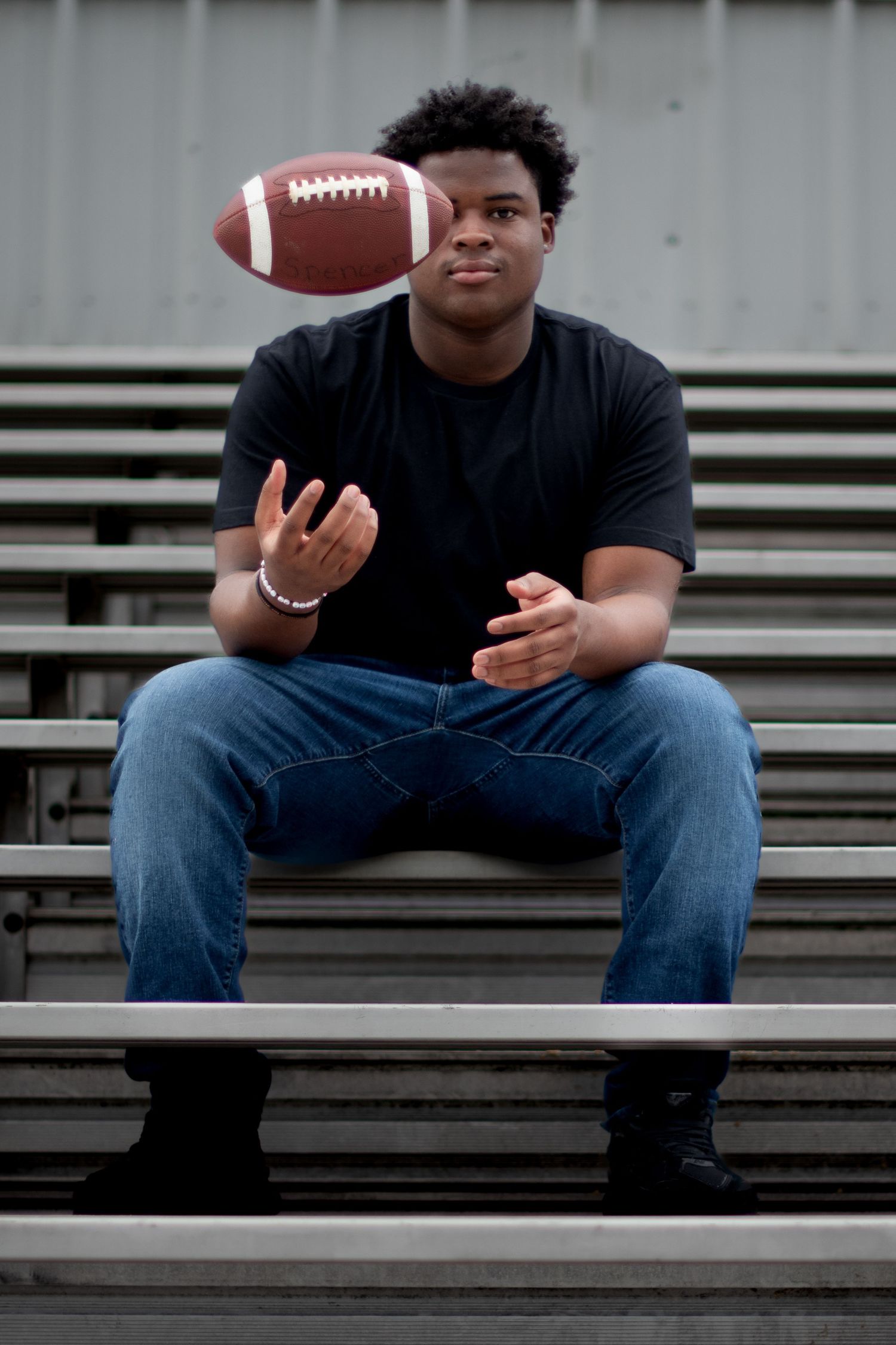Athletic person in dark shirt sitting on bleachers playing with a football.