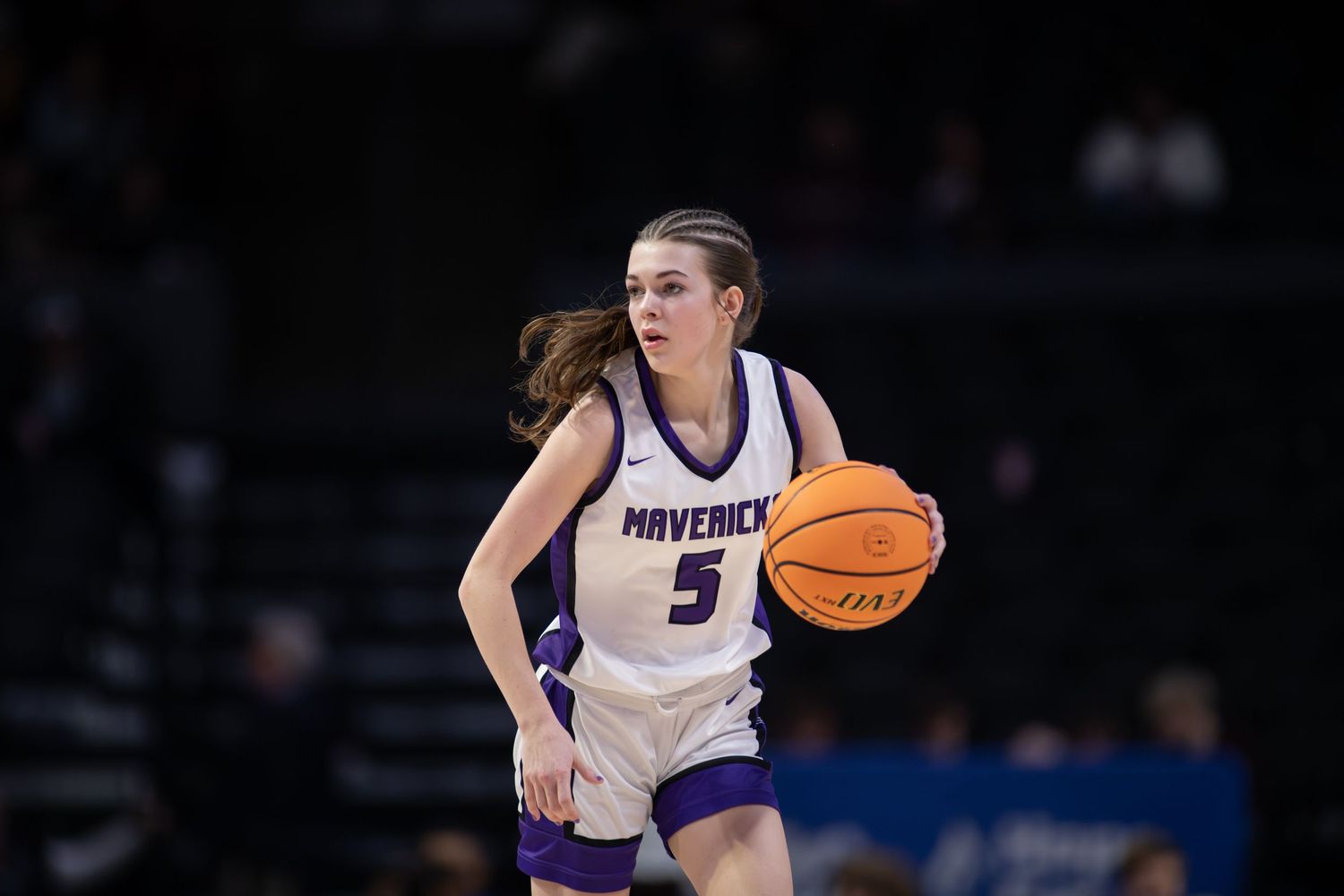 Basketball player in white and purple uniform dribbles the ball during an intense game on the court.