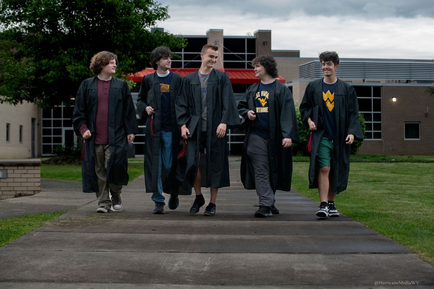 Graduates walking together in caps and gowns on a cloudy day.