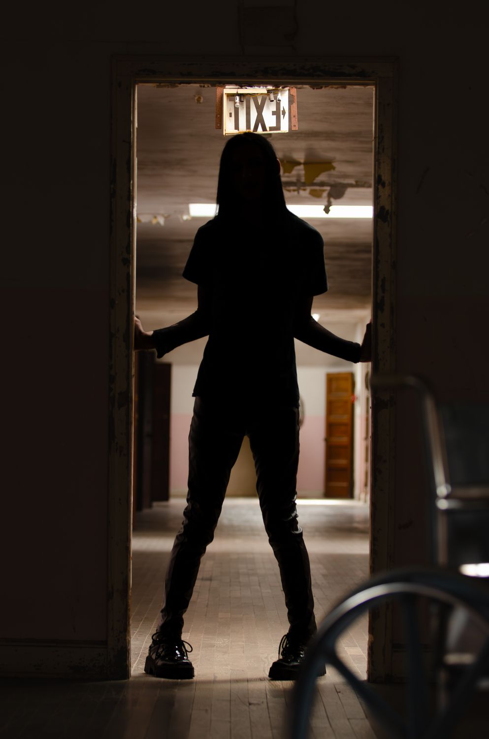 Silhouette of a person standing in a dark doorway with an exit sign visible above.