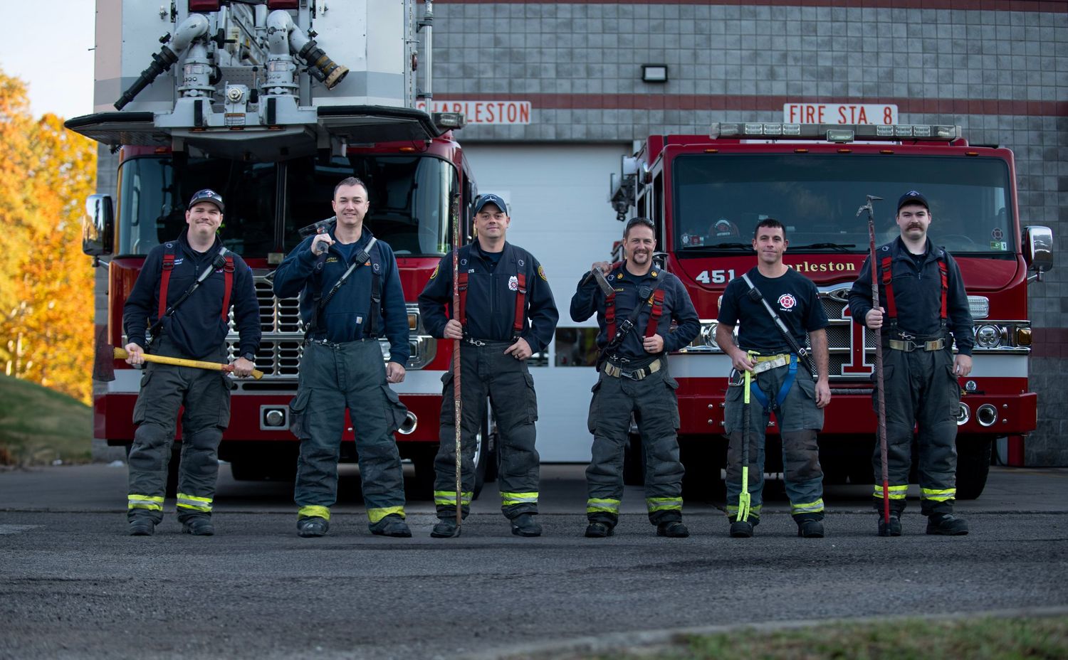 Line of firefighters in uniform sitting together outside fire station at dusk.