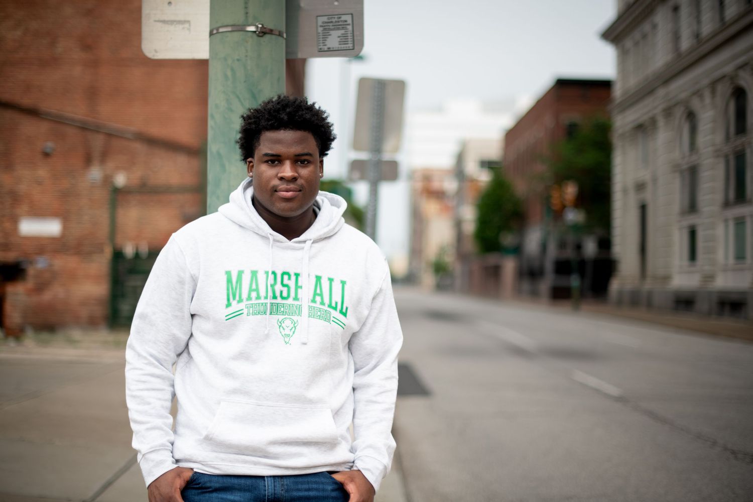 A student wearing a Marshall University sweatshirt stands on an urban street.