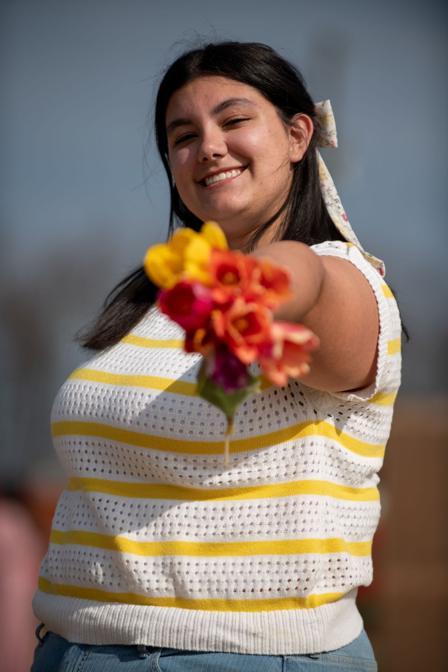 Person in striped sweater holding colorful flowers on a sunny day.