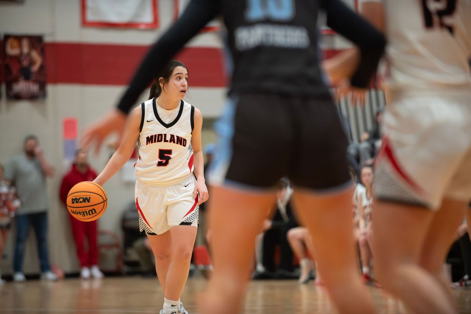 Basketball player in white Notre Dame jersey dribbles the ball during a game against opponent in black uniform.