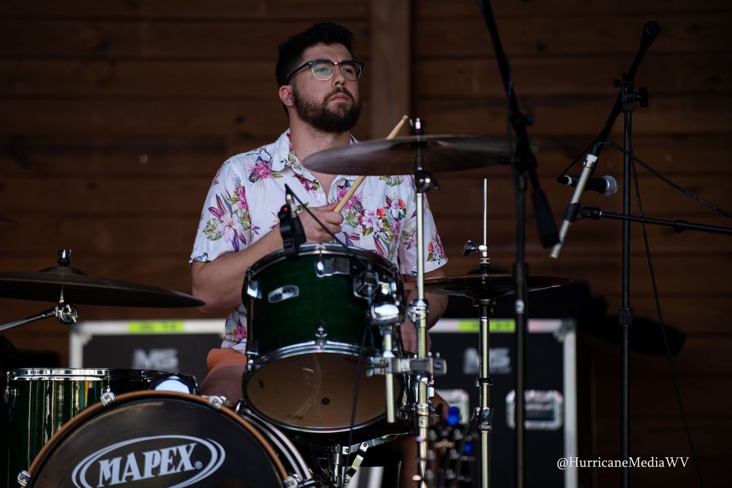 A drummer performs energetically behind a Mapex drum kit on stage during a live performance.