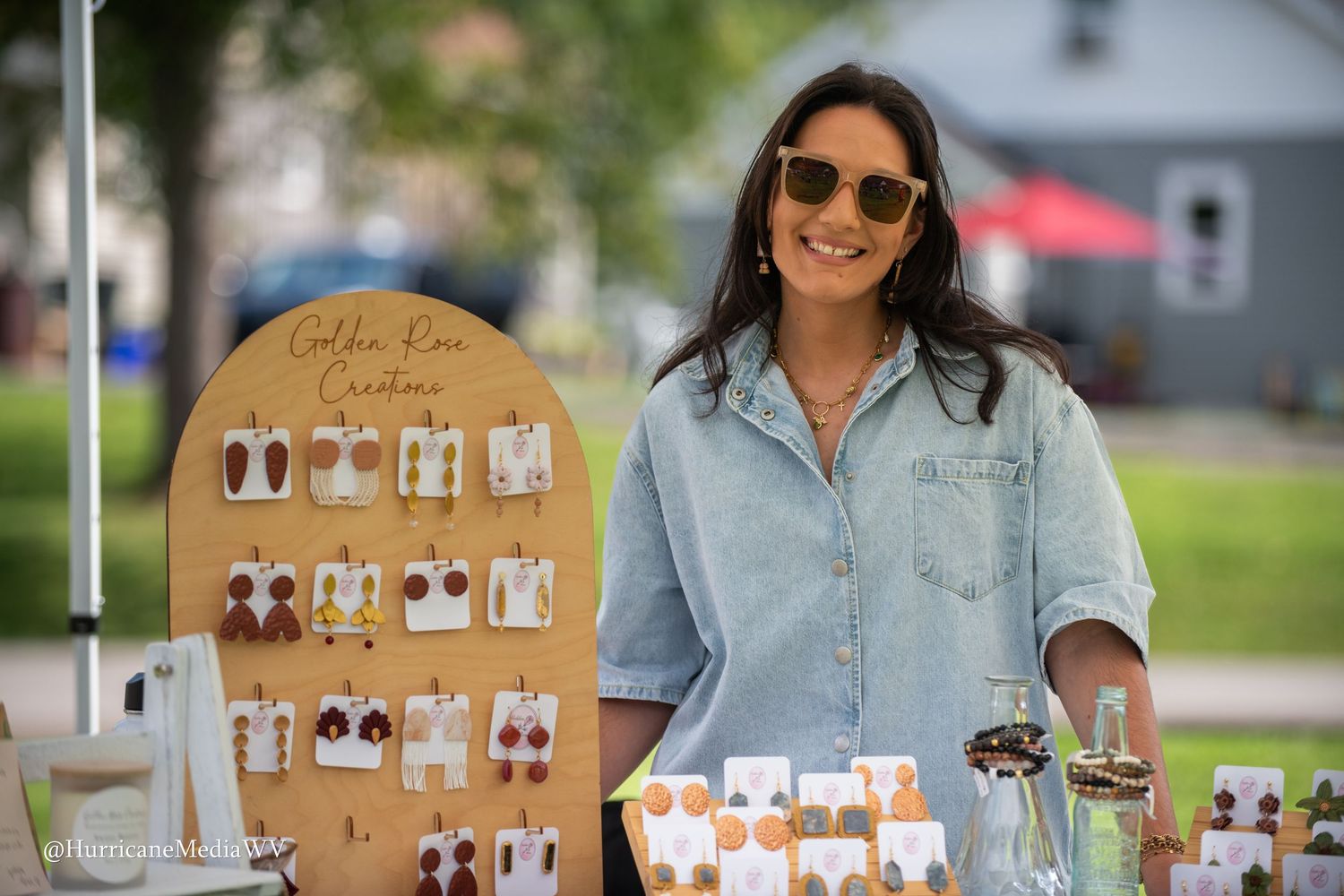 Wooden earring display stand showcasing handmade jewelry at an outdoor artisan market or craft fair.