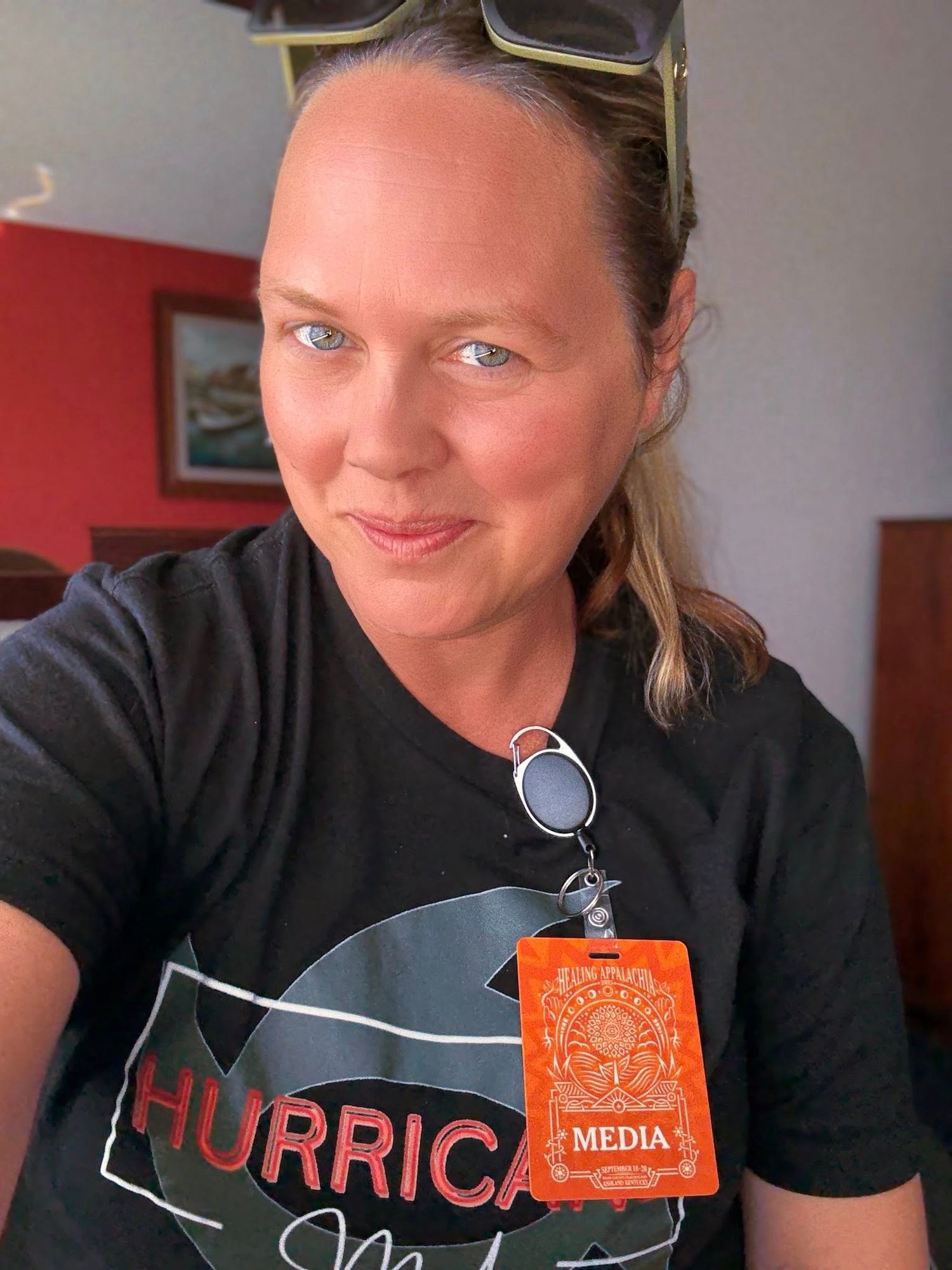 A selfie showing someone wearing a black t-shirt with a hurricane design and an orange media badge around their neck.