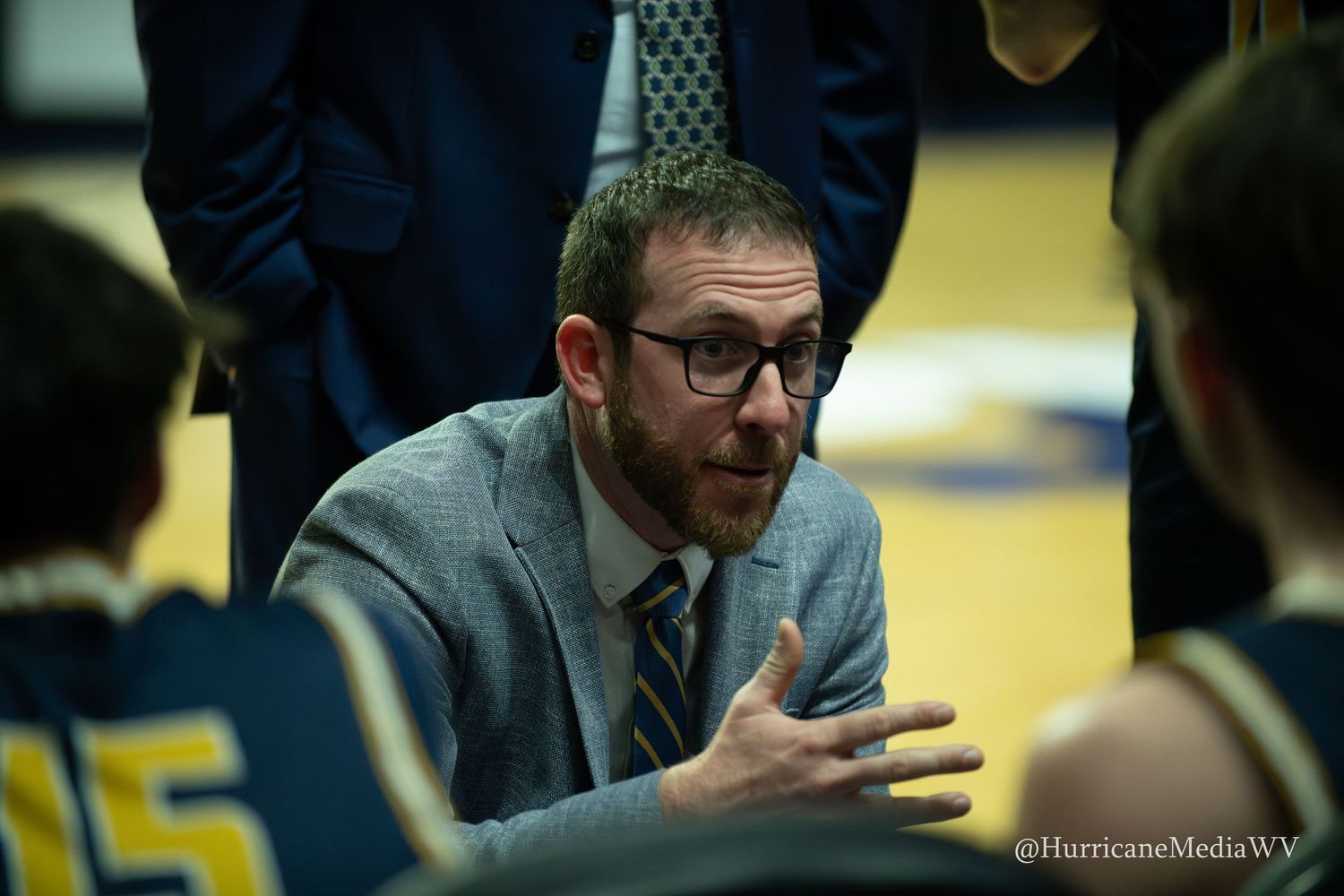 A basketball coach gestures animatedly during a game while standing on the sidelines.