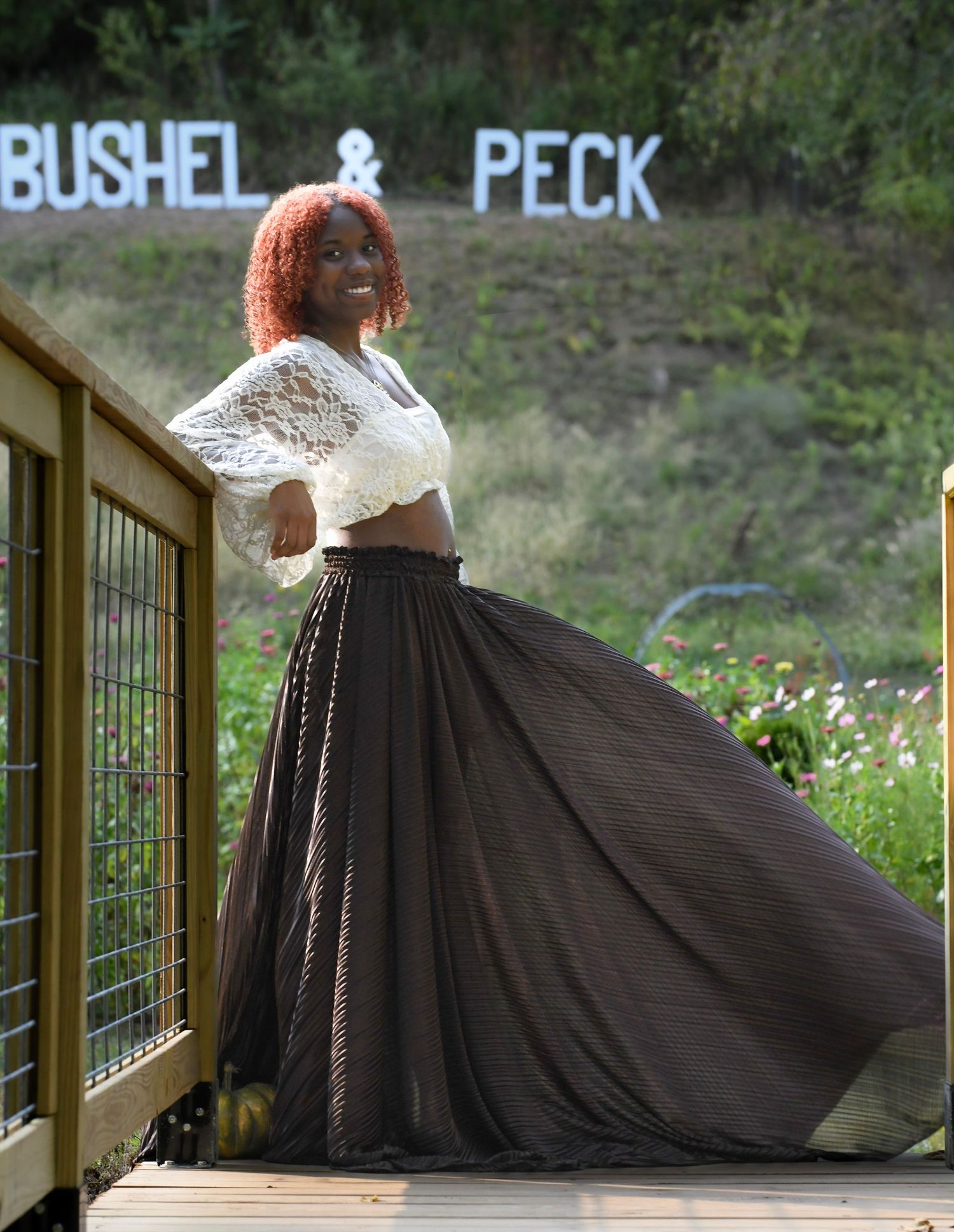 A dramatic portrait on a deck with 'Bushel & Peck' signage featuring a flowing black skirt and lace top.