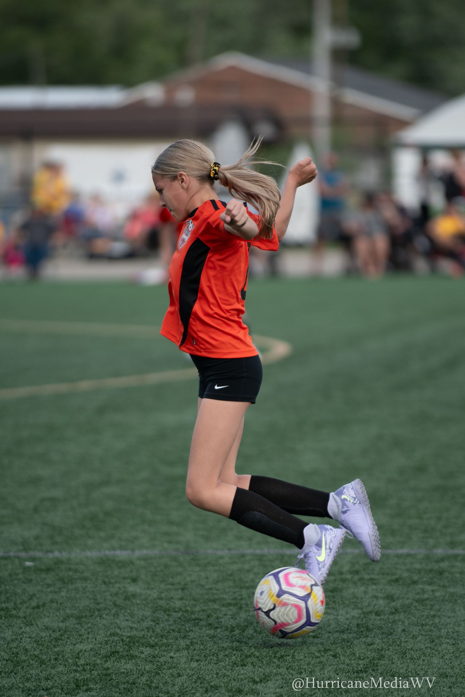Soccer player in orange jersey kicks ball on artificial turf field during game action.