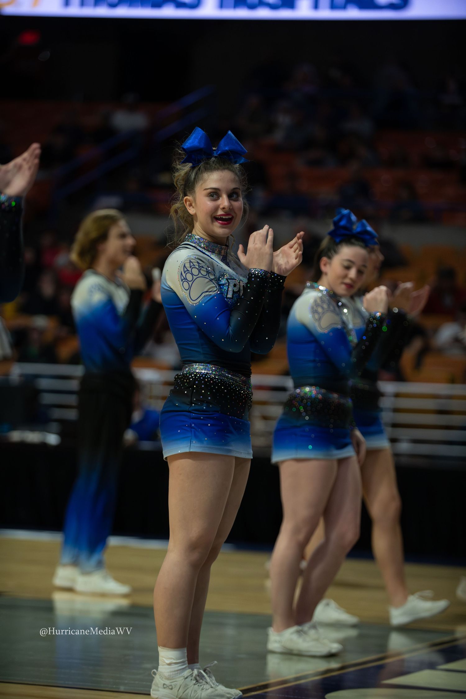 Cheerleaders in blue uniforms perform synchronized dance routine on basketball court during halftime show.
