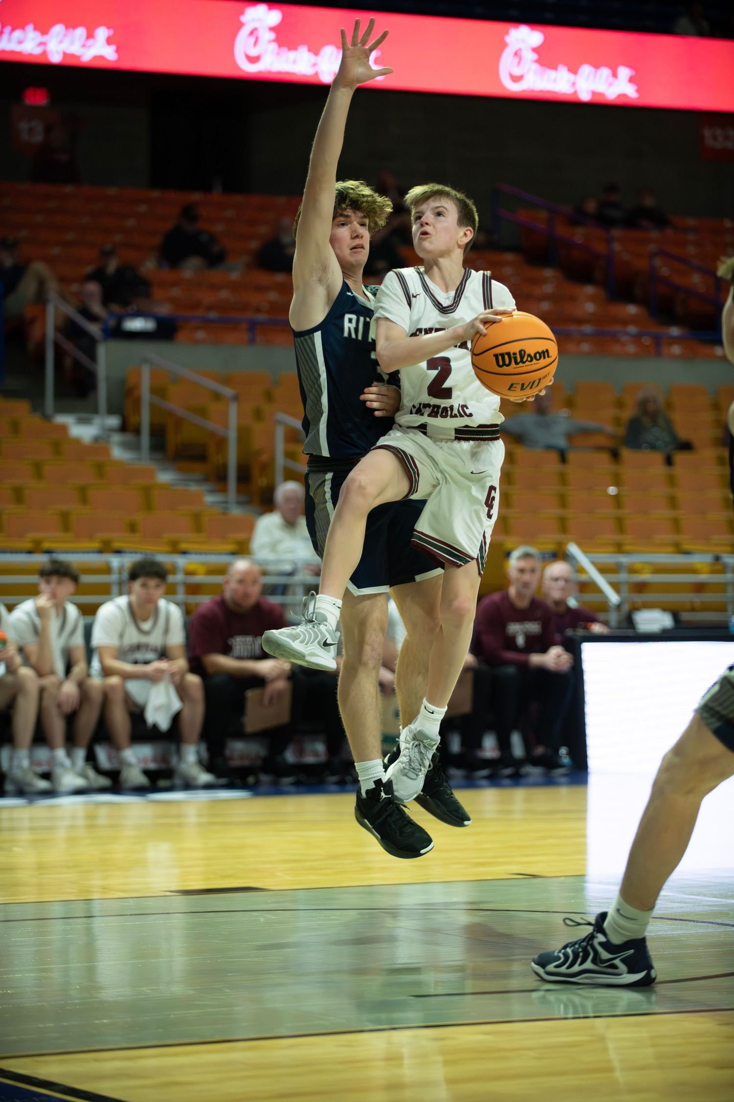 Basketball player drives to the hoop while defender attempts to block the shot during game action.
