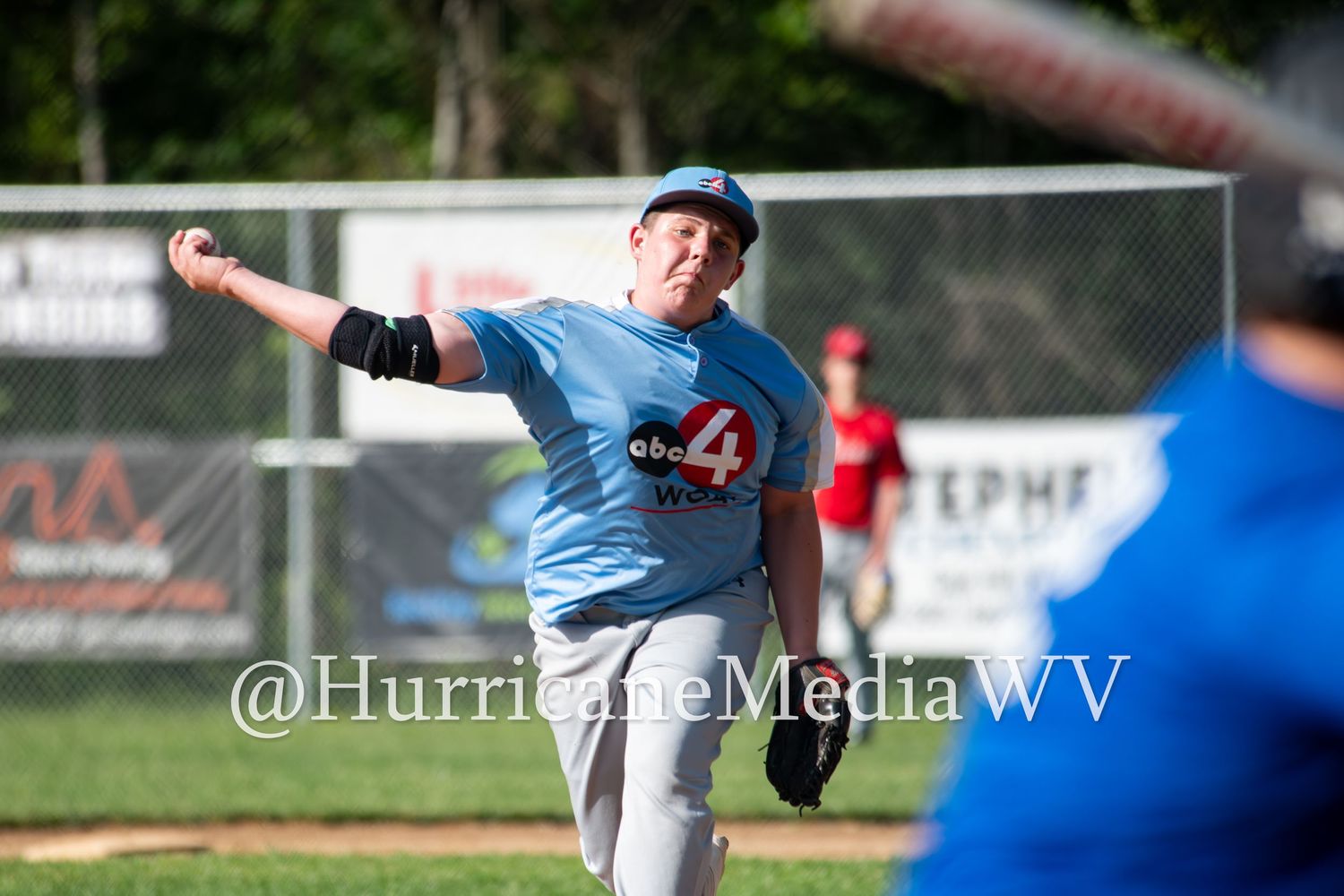 Baseball pitcher in light blue uniform mid-throw during game action.