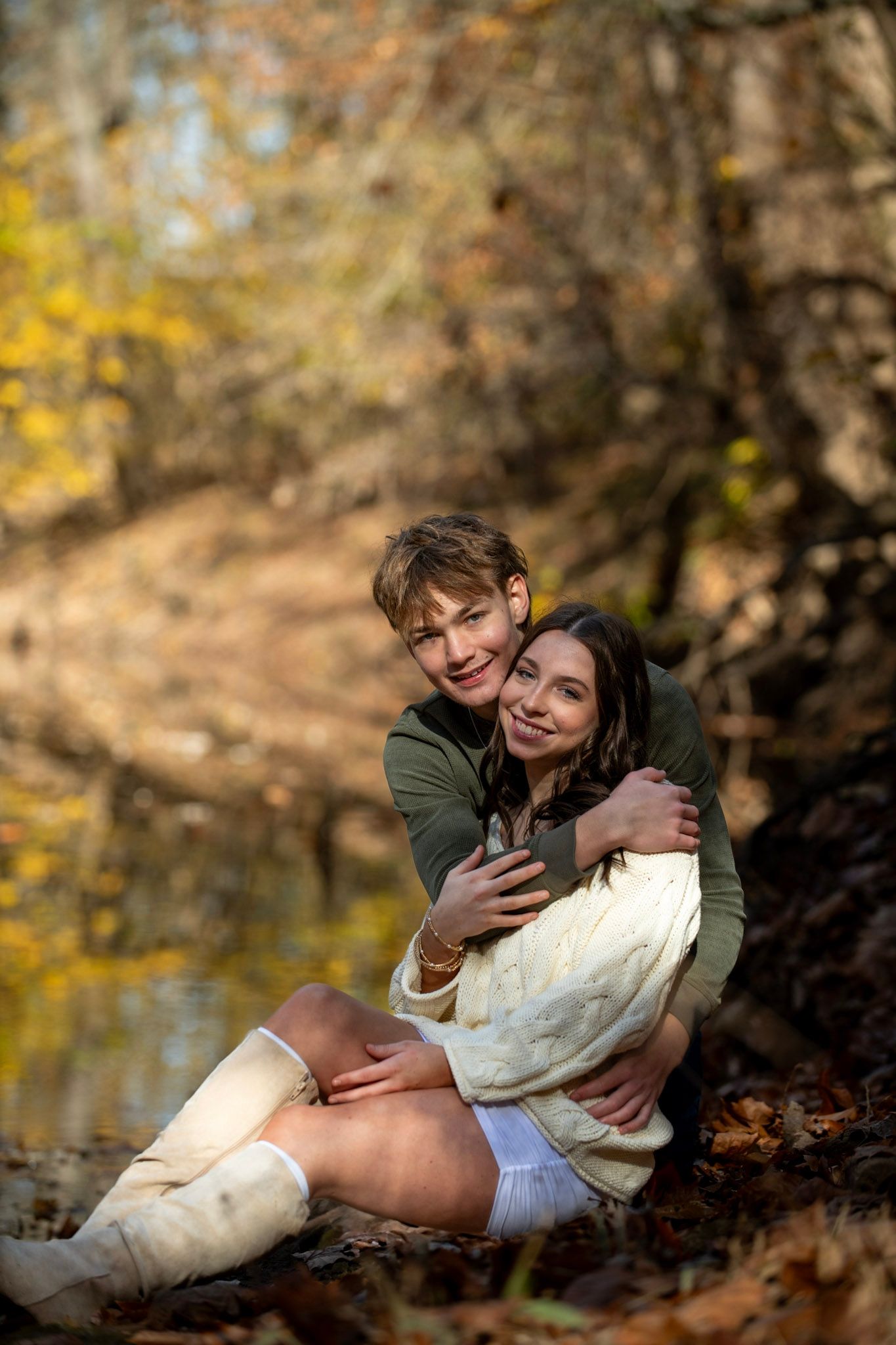 A couple shares an intimate moment among fallen autumn leaves by a stream.
