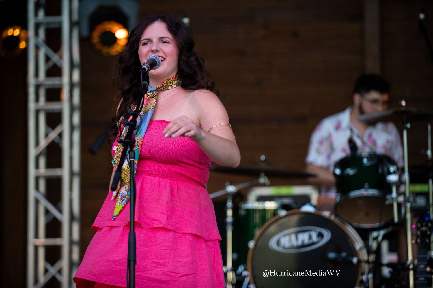 A performer in a bright pink dress sings passionately into a microphone on stage during a live music performance.