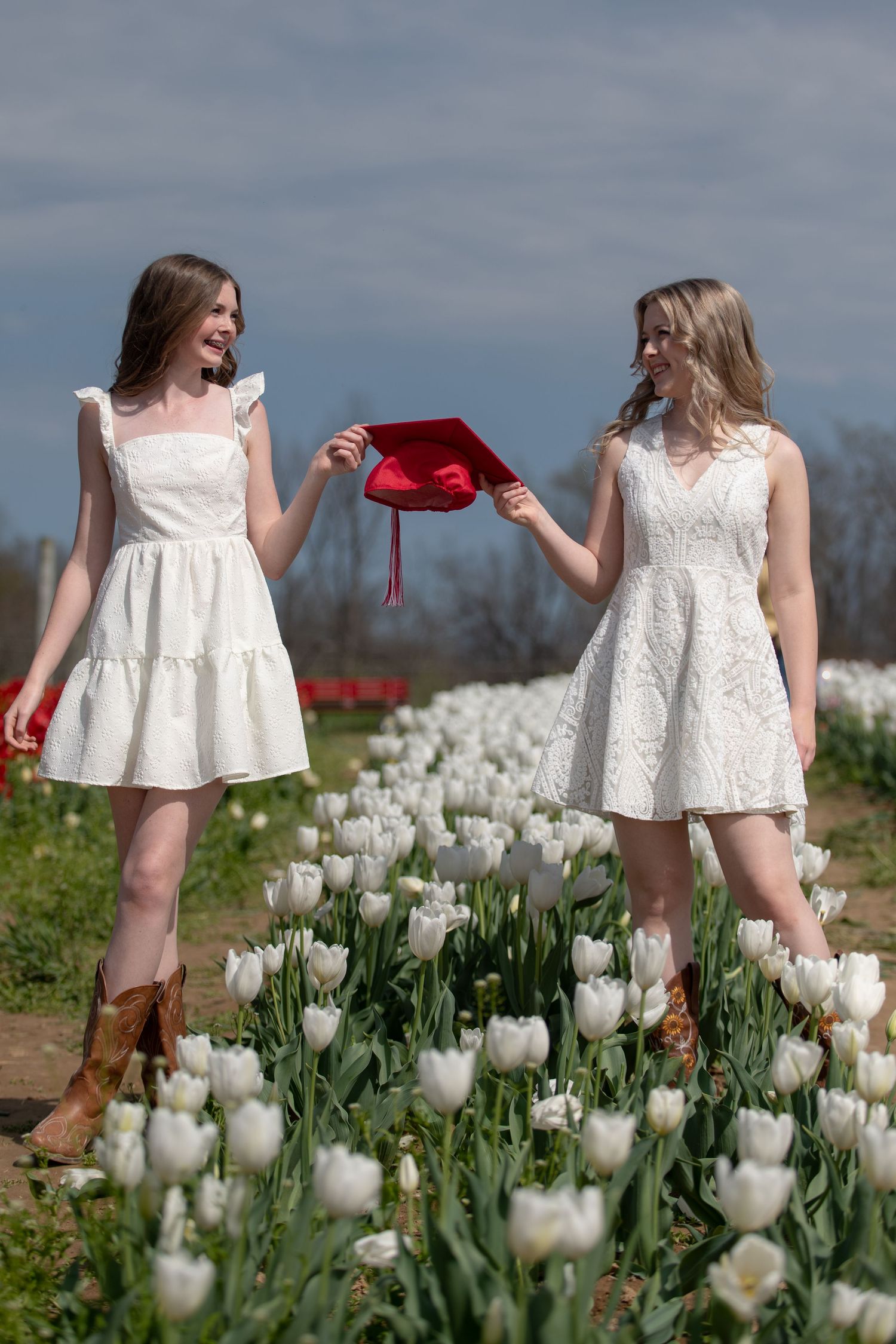 Two people in white dresses stand in a field of white tulips while holding a red garment between them.