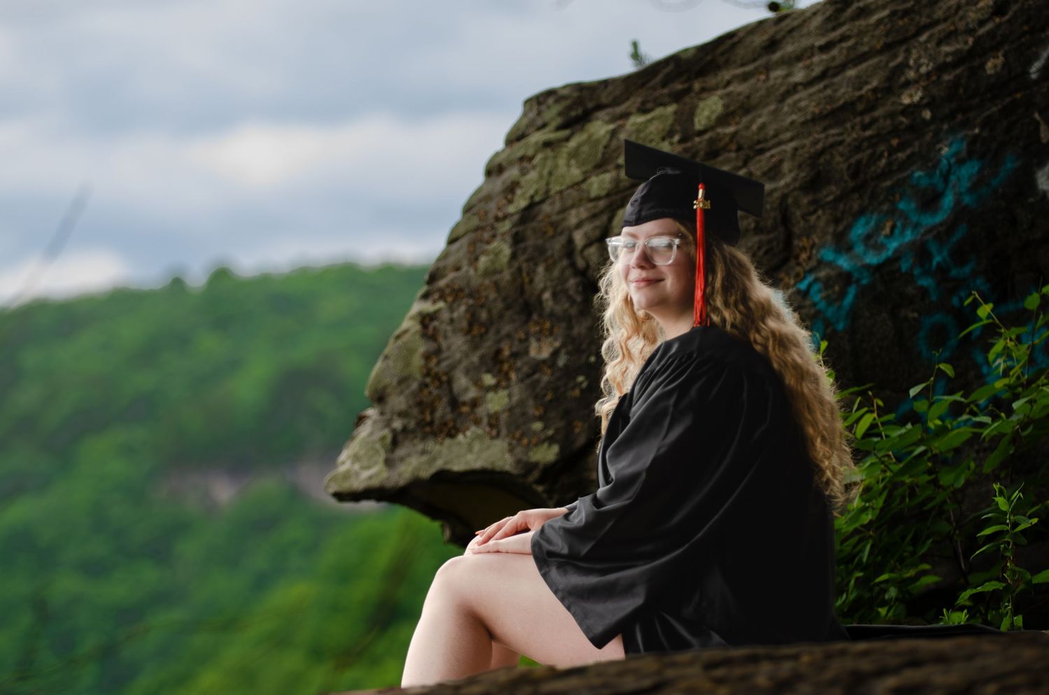A graduation portrait captured on a rocky cliff overlooking a scenic mountain landscape.