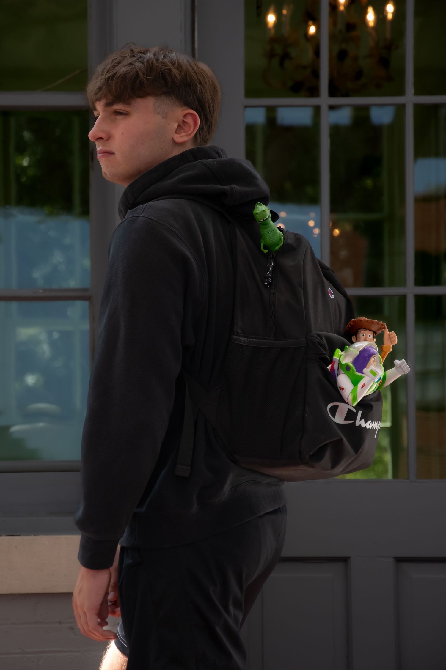 Someone in a black hoodie stands near a window with hanging lights inside a dark room at night.