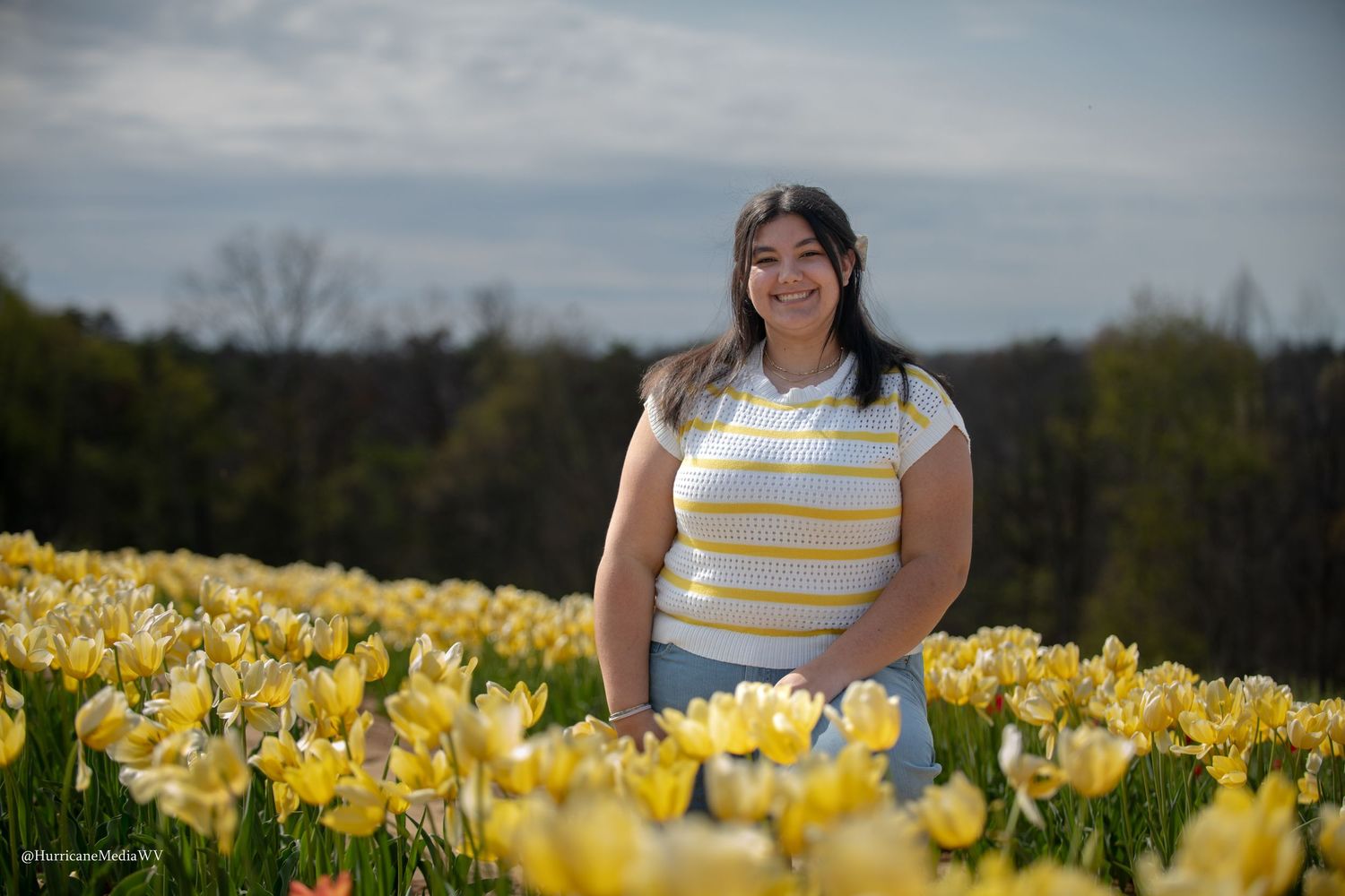 Person posing in a vibrant yellow daffodil field on a sunny spring day.