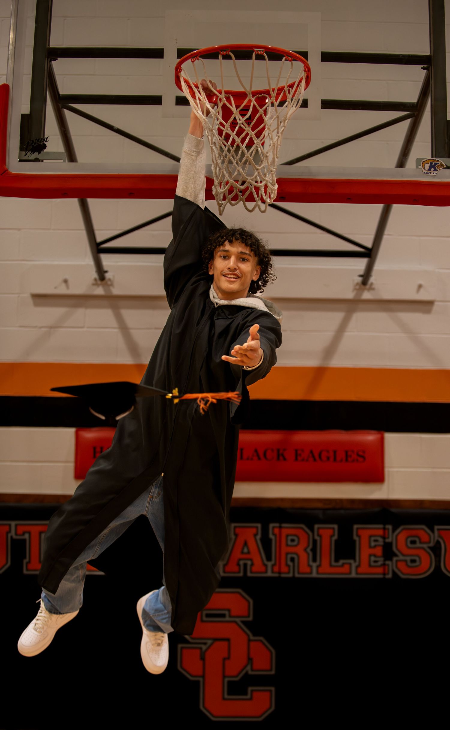 Basketball player hangs from rim after slam dunk in gymnasium.