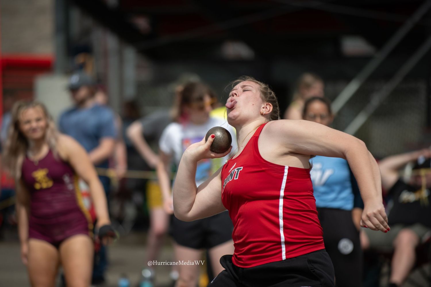 Athlete in red uniform competing in shot put event at track meet.