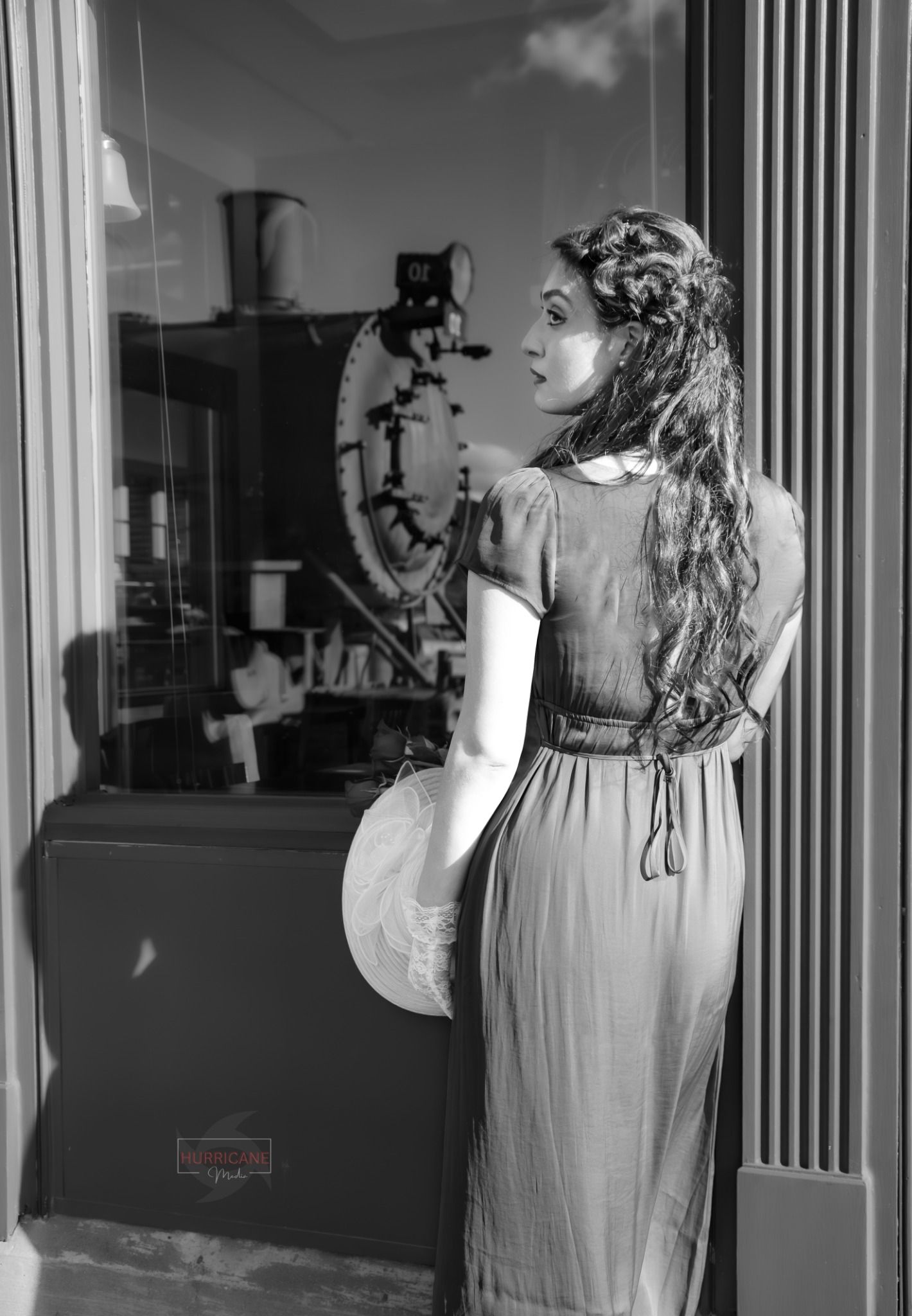 Vintage black and white portrait showing a woman in a long dress looking at a cat in a window display.