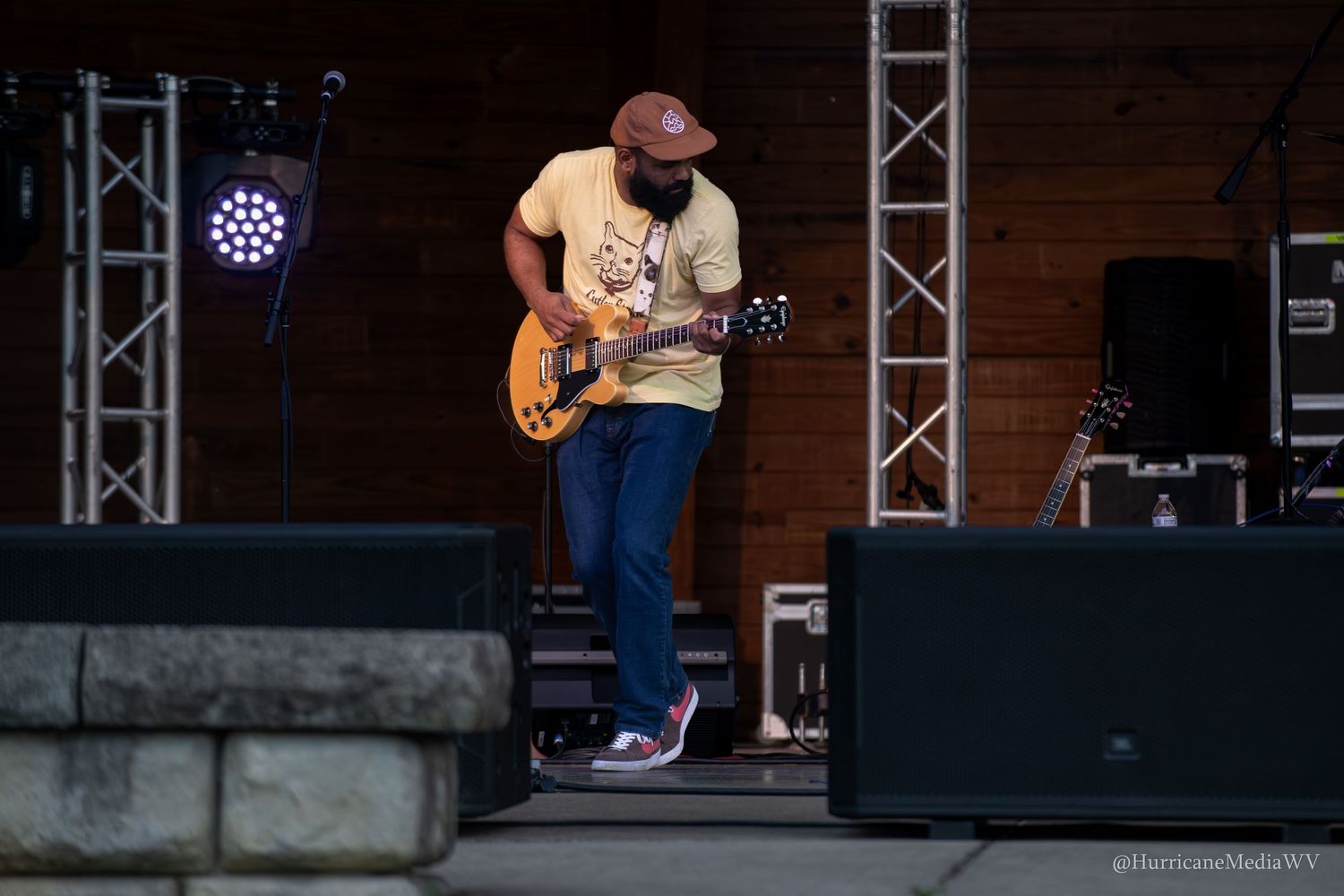 Musicians perform on an outdoor concert stage with lighting rigs and guitar players visible on the platform.