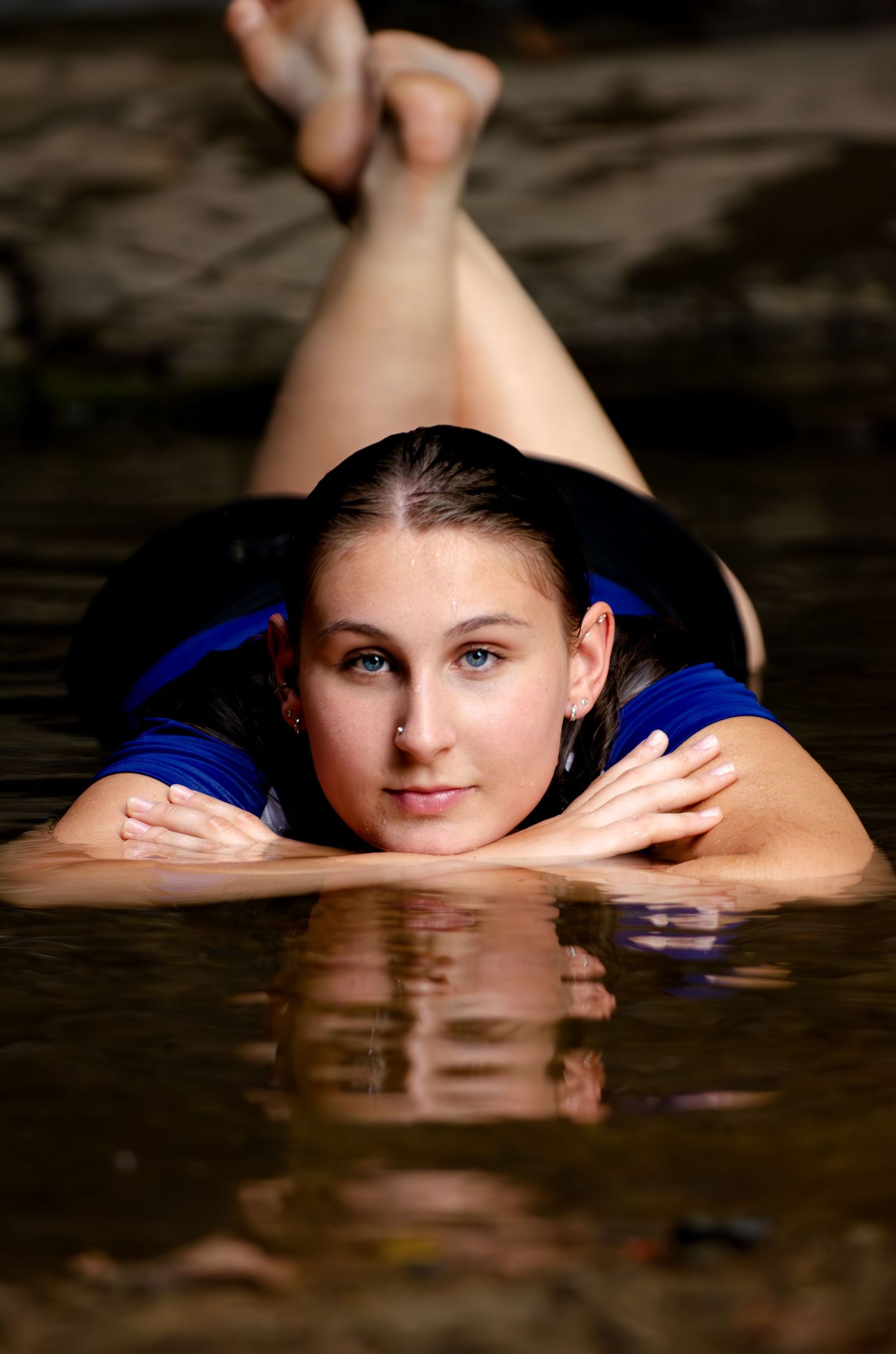 A reflective portrait in a blue dress laying on a dark surface with water creating a mirror effect.