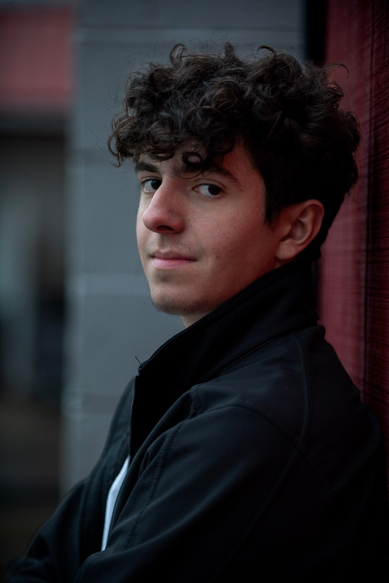A moody portrait featuring someone in a black jacket against a red wall.