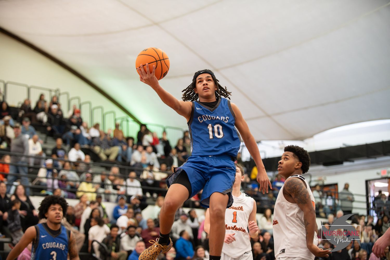 Basketball player in blue jersey number 10 soars high for a dunk during an indoor game with spectators watching.