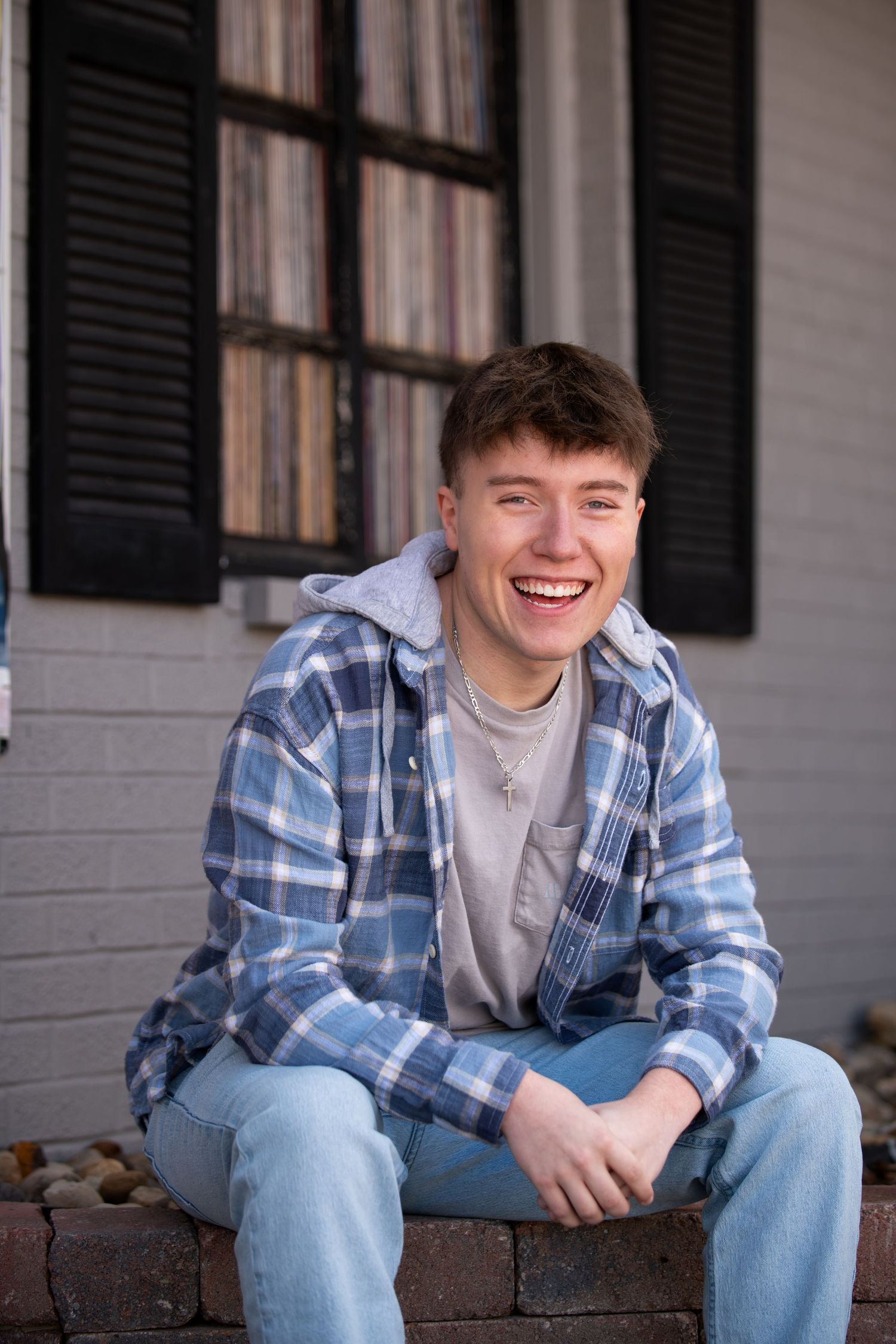 Portrait of someone in a blue plaid flannel shirt and jeans sitting on brick steps with a bright smile.