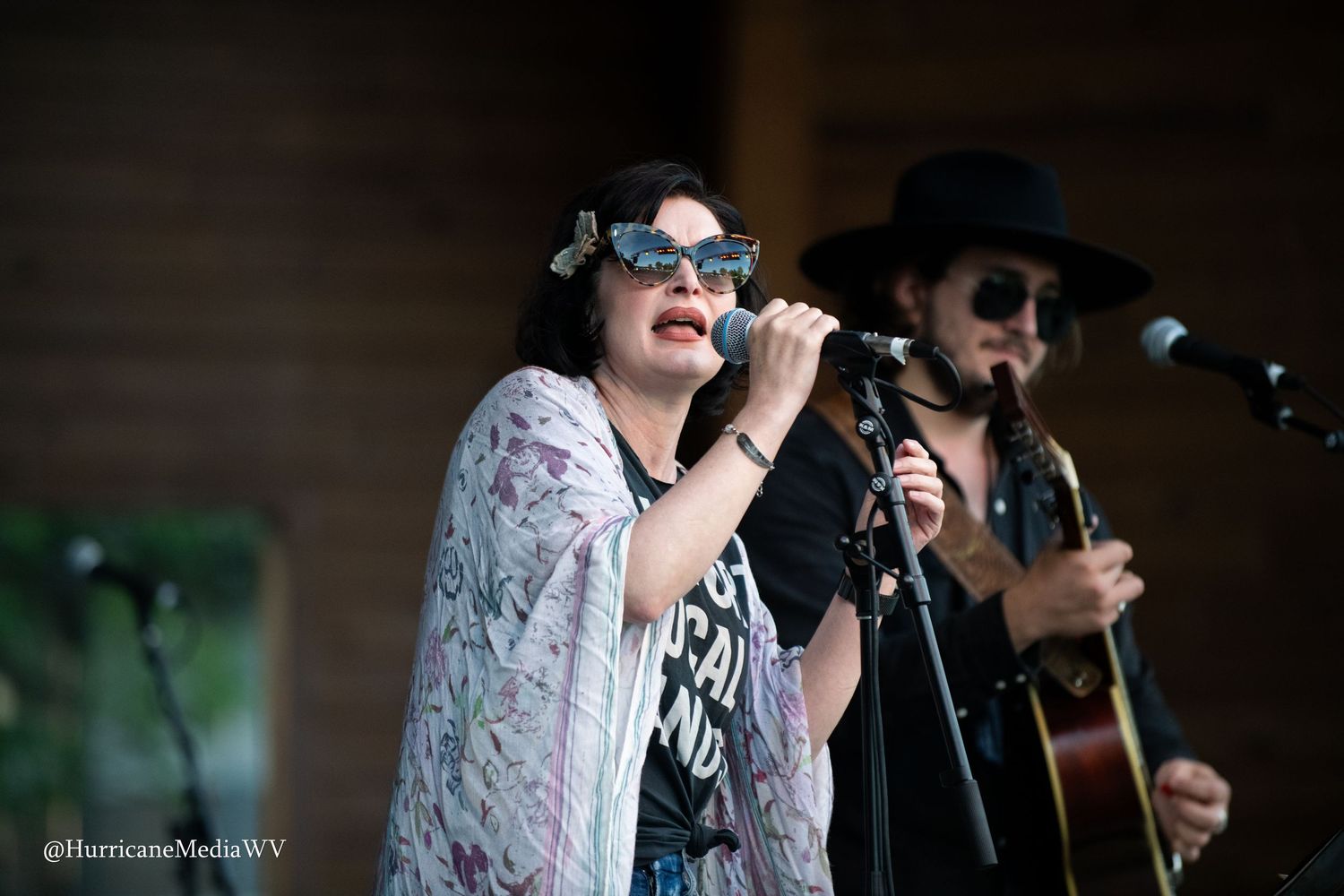 Two performers singing together on stage with microphones during a live musical performance outdoors.