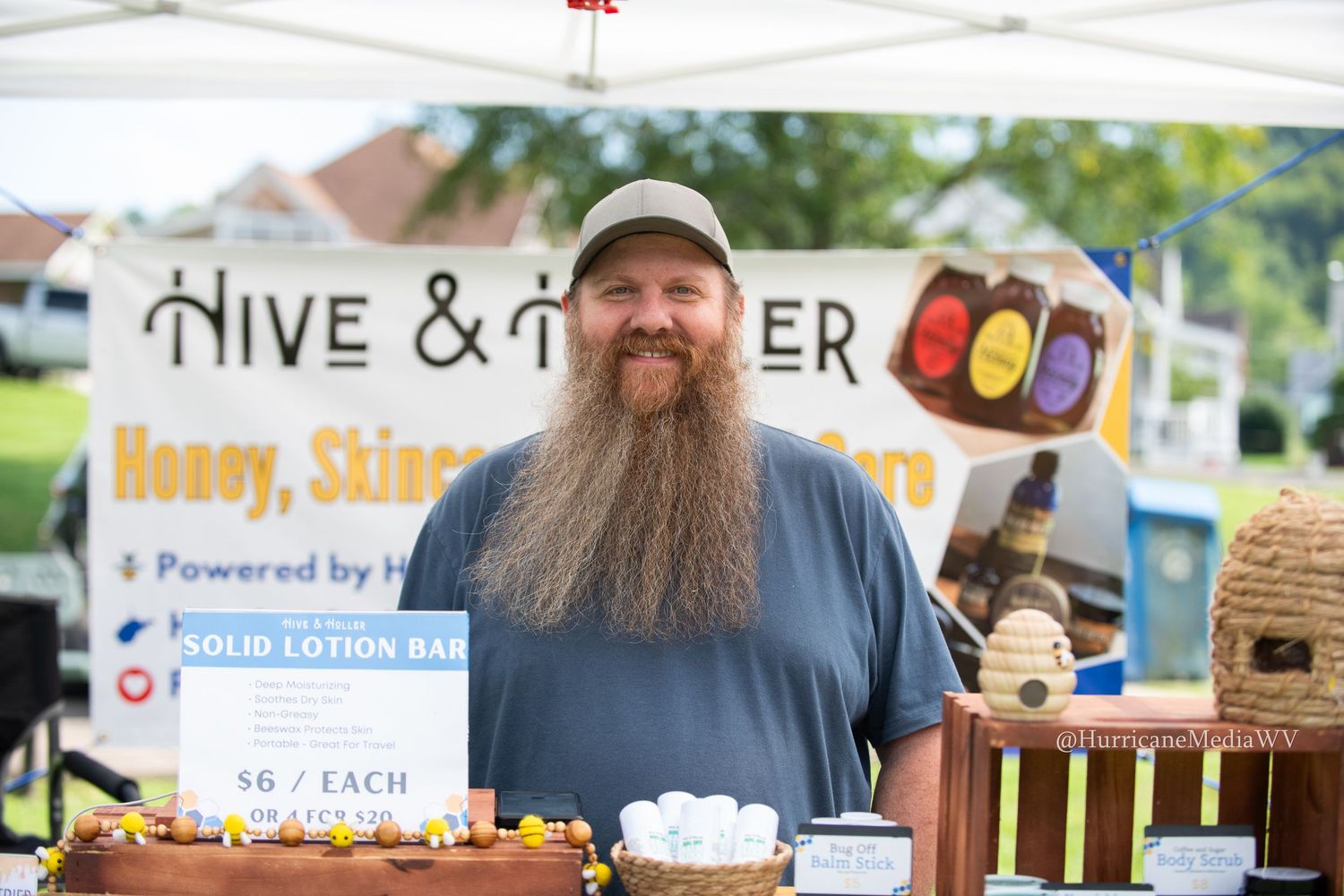 A row of outdoor vendor booths at a farmers market selling honey, cotton candy and various local products.
