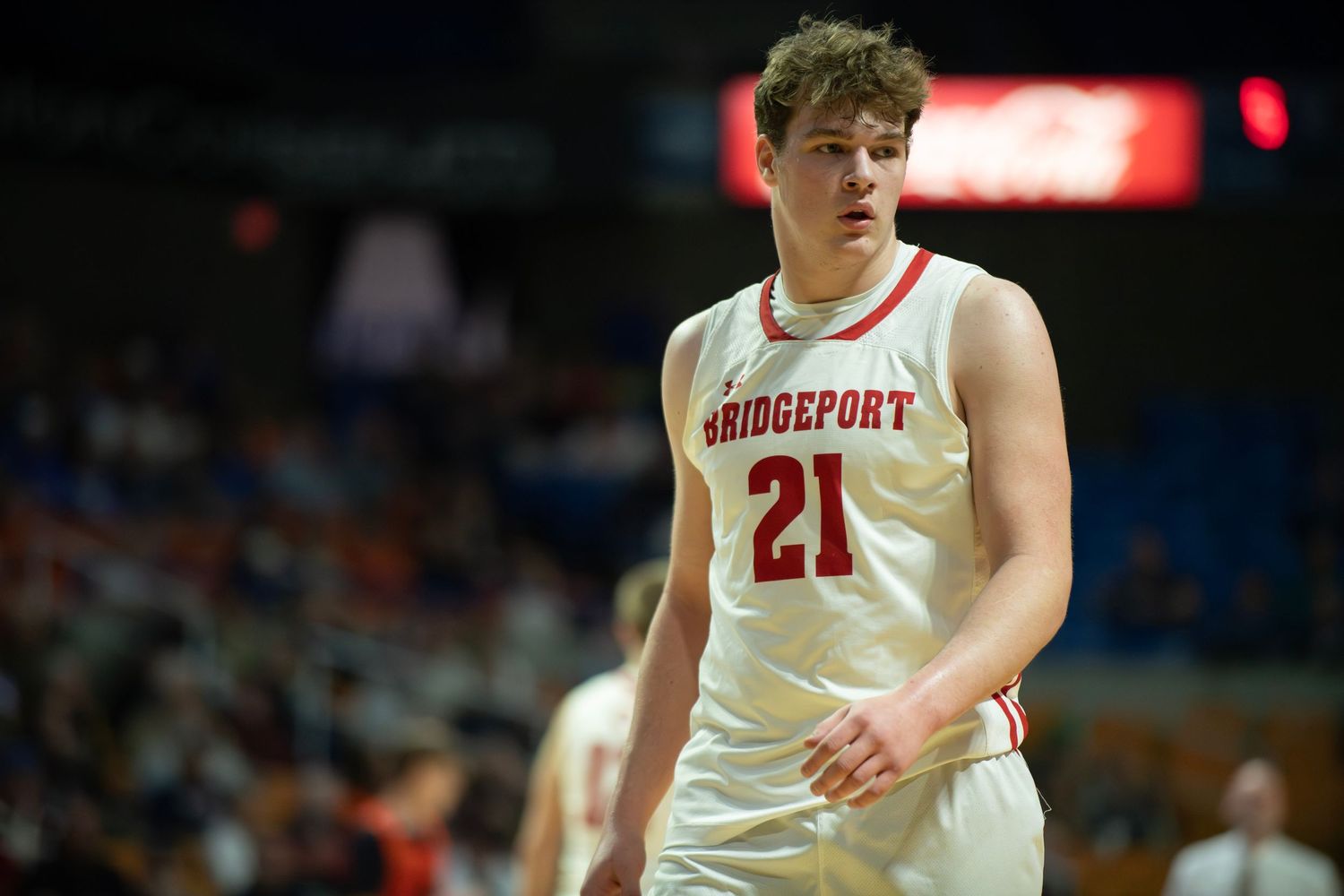 Basketball player in white Bridgeport jersey number 21 plays in arena game.