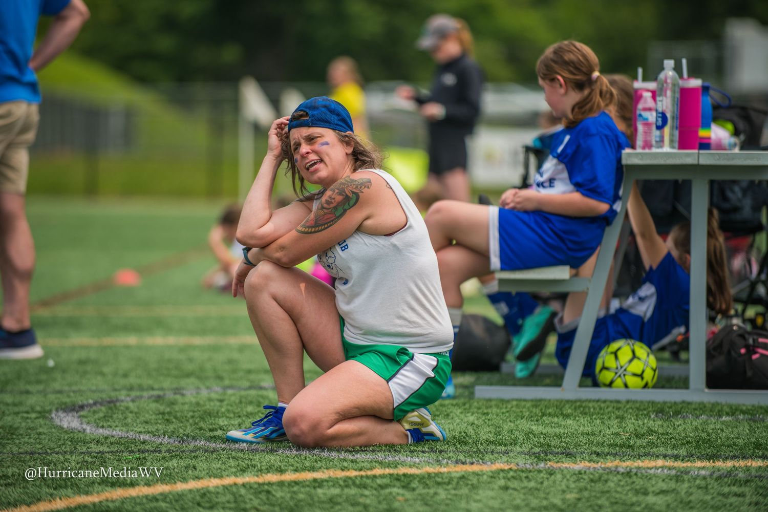 Spectators watching from sidelines of outdoor sports field with benches and equipment visible.
