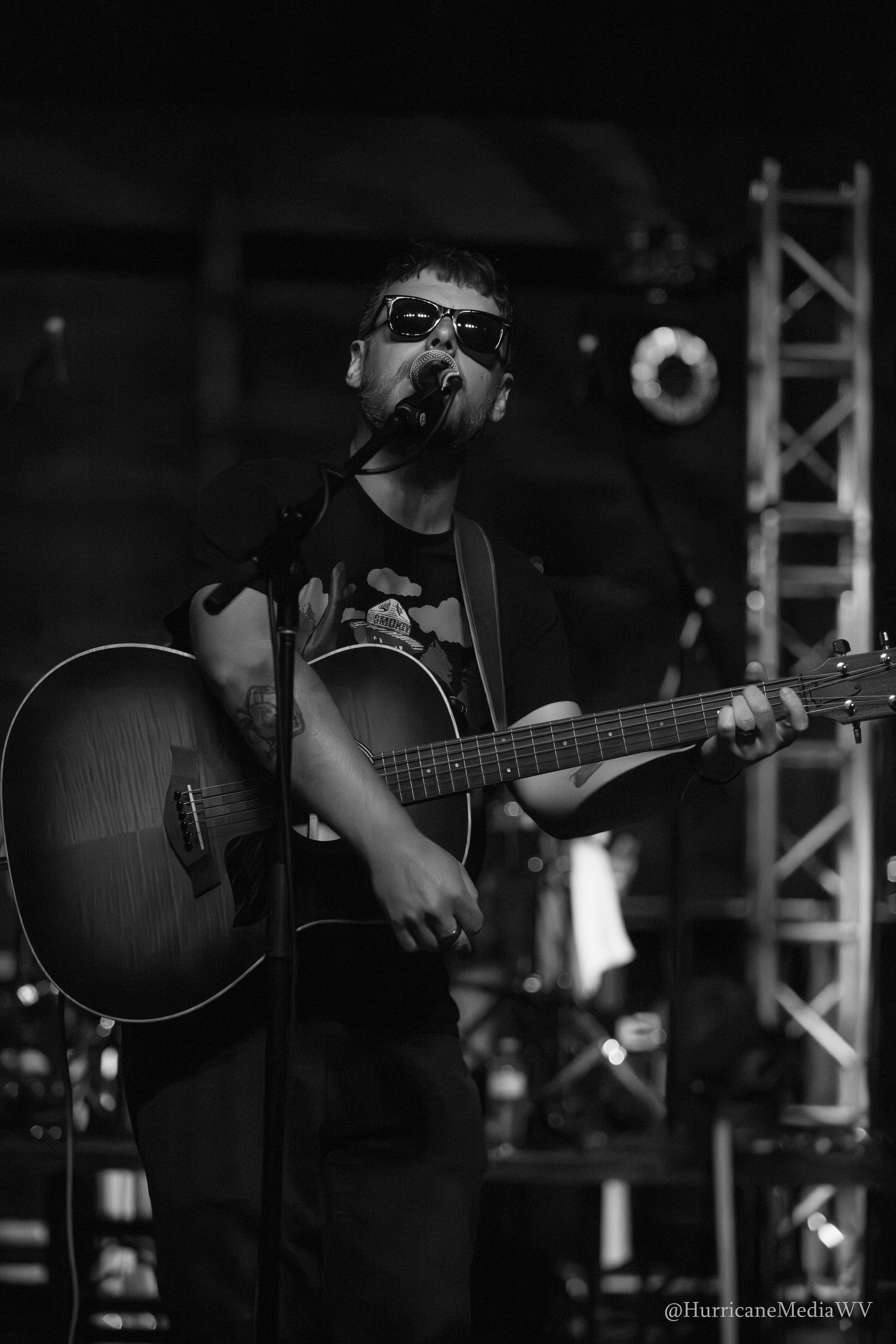 Musician performs on stage with acoustic guitar in monochromatic black and white lighting during live concert.